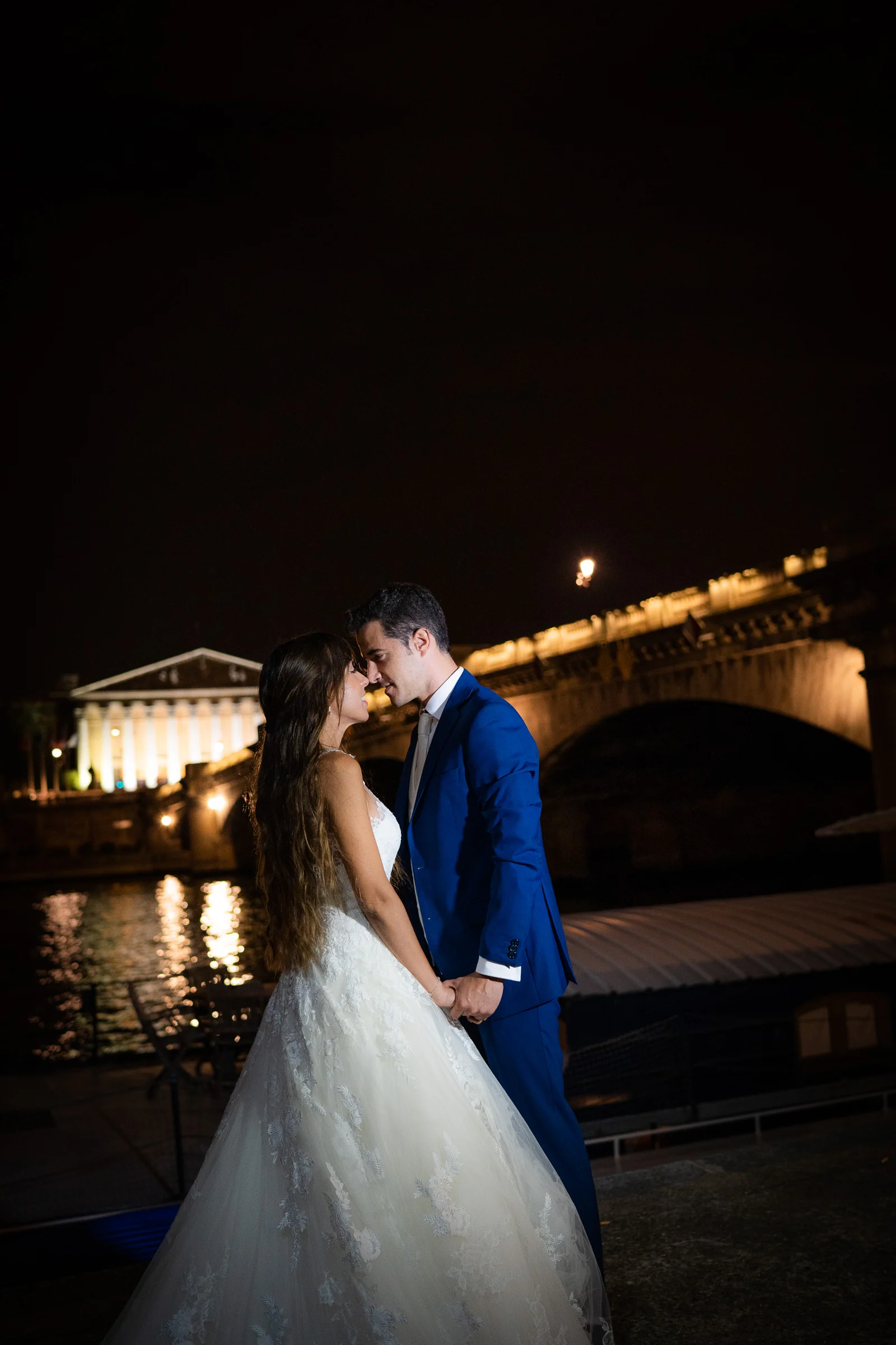 José Luis y Lara se miran junto al Sena de noche con un puente iluminado al fondo.