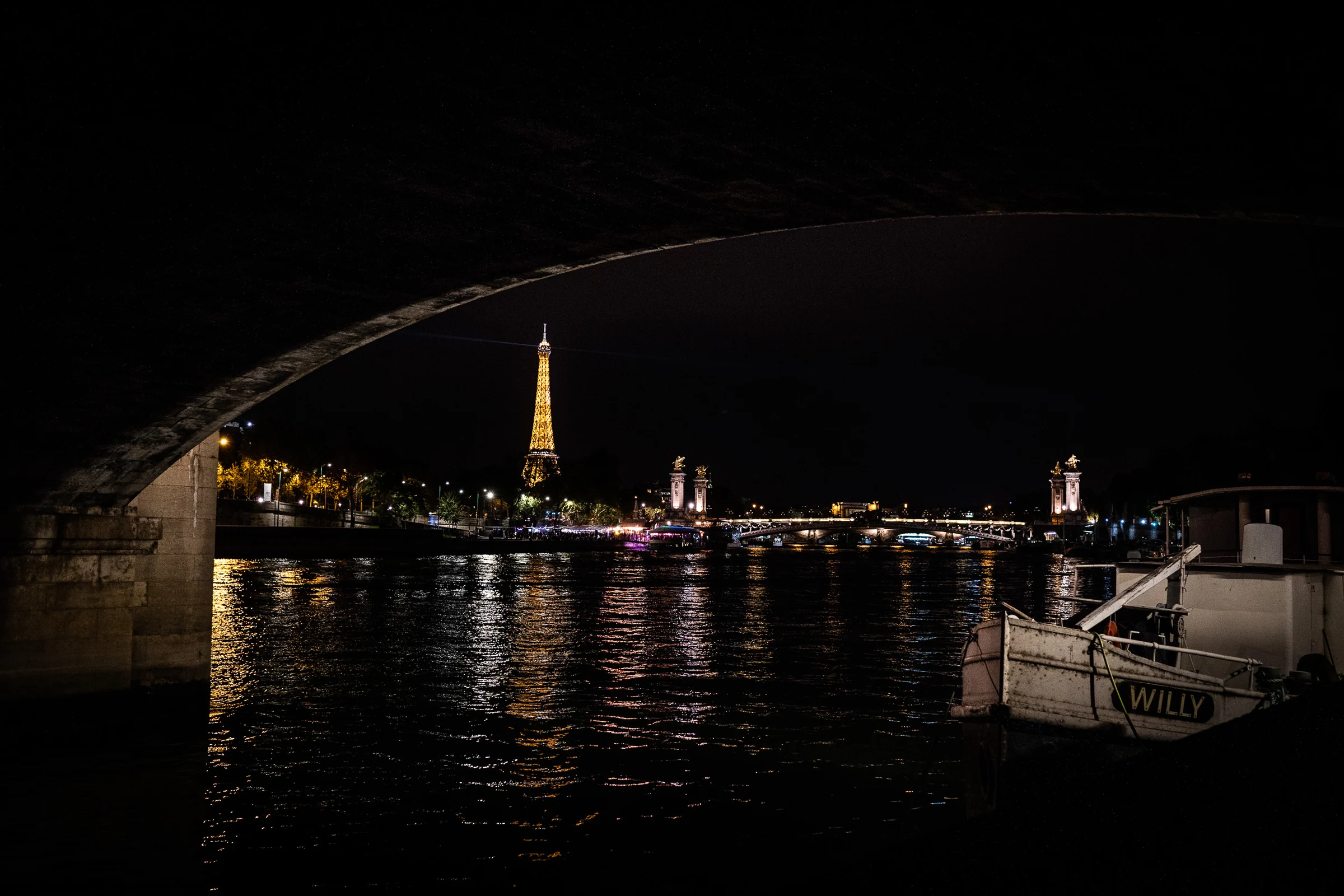 Vista nocturna del Sena con la Torre Eiffel iluminada al fondo y un barco amarrado en primer plano.