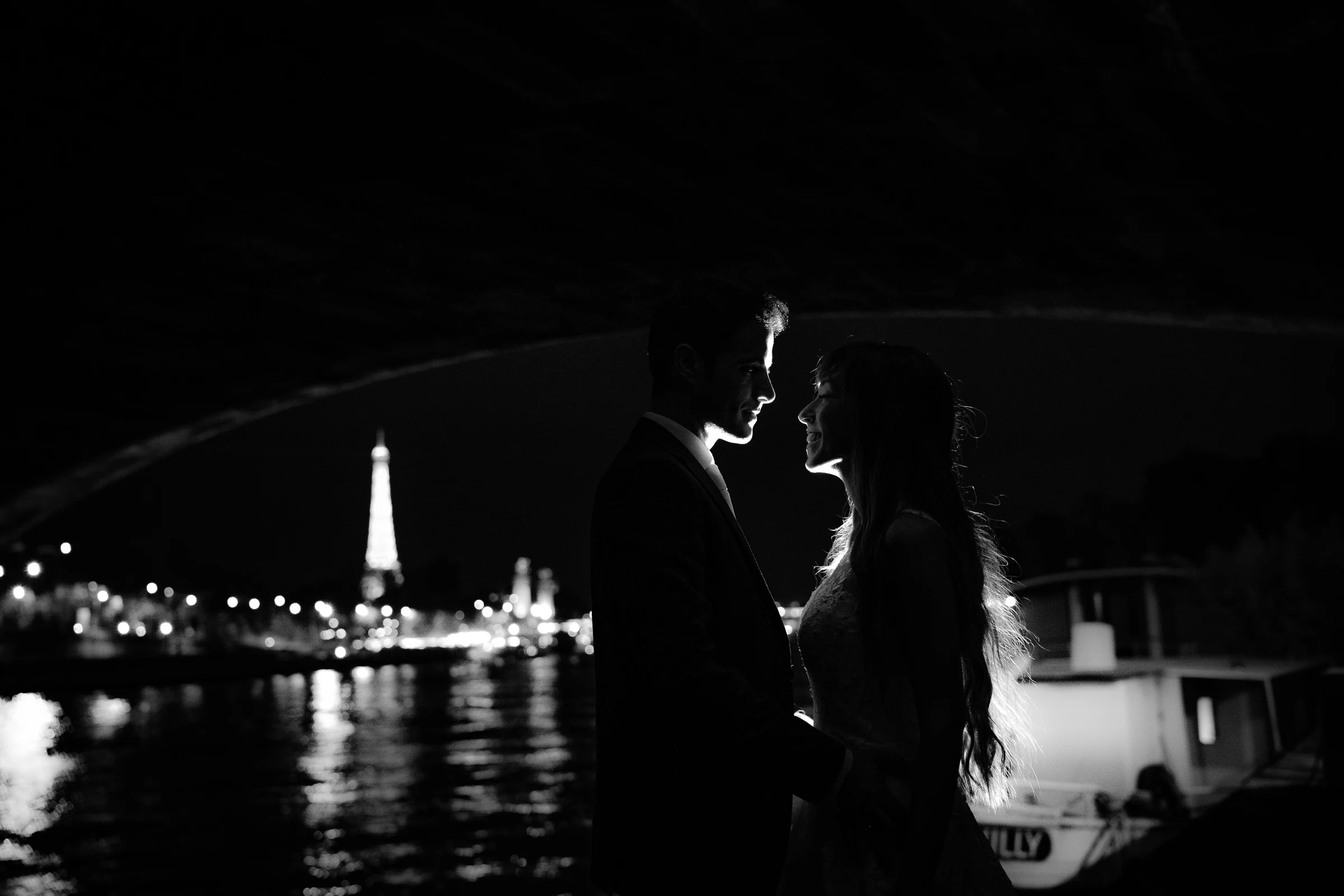 Silueta en blanco y negro de José Luis y Lara bajo un puente con la Torre Eiffel iluminada al fondo.