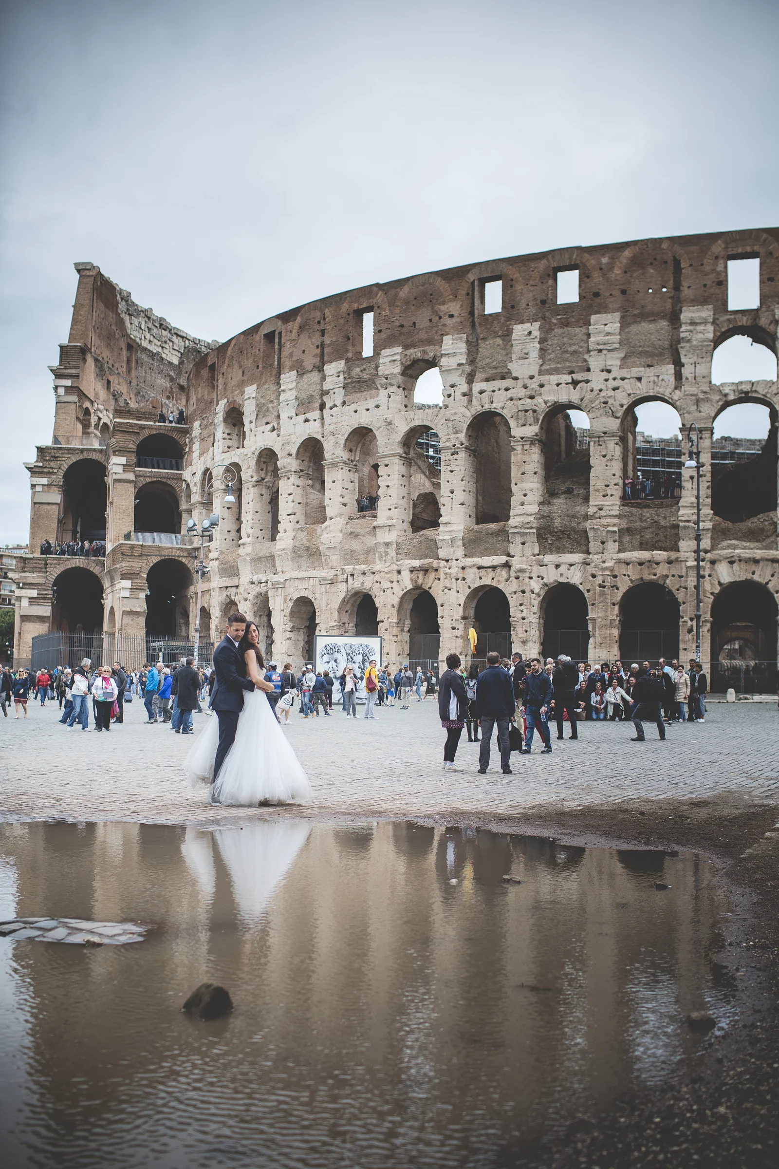 Los novios frente al Coliseo con el monumento reflejado en un gran charco durante una sesión postboda en Coliseo de Roma.