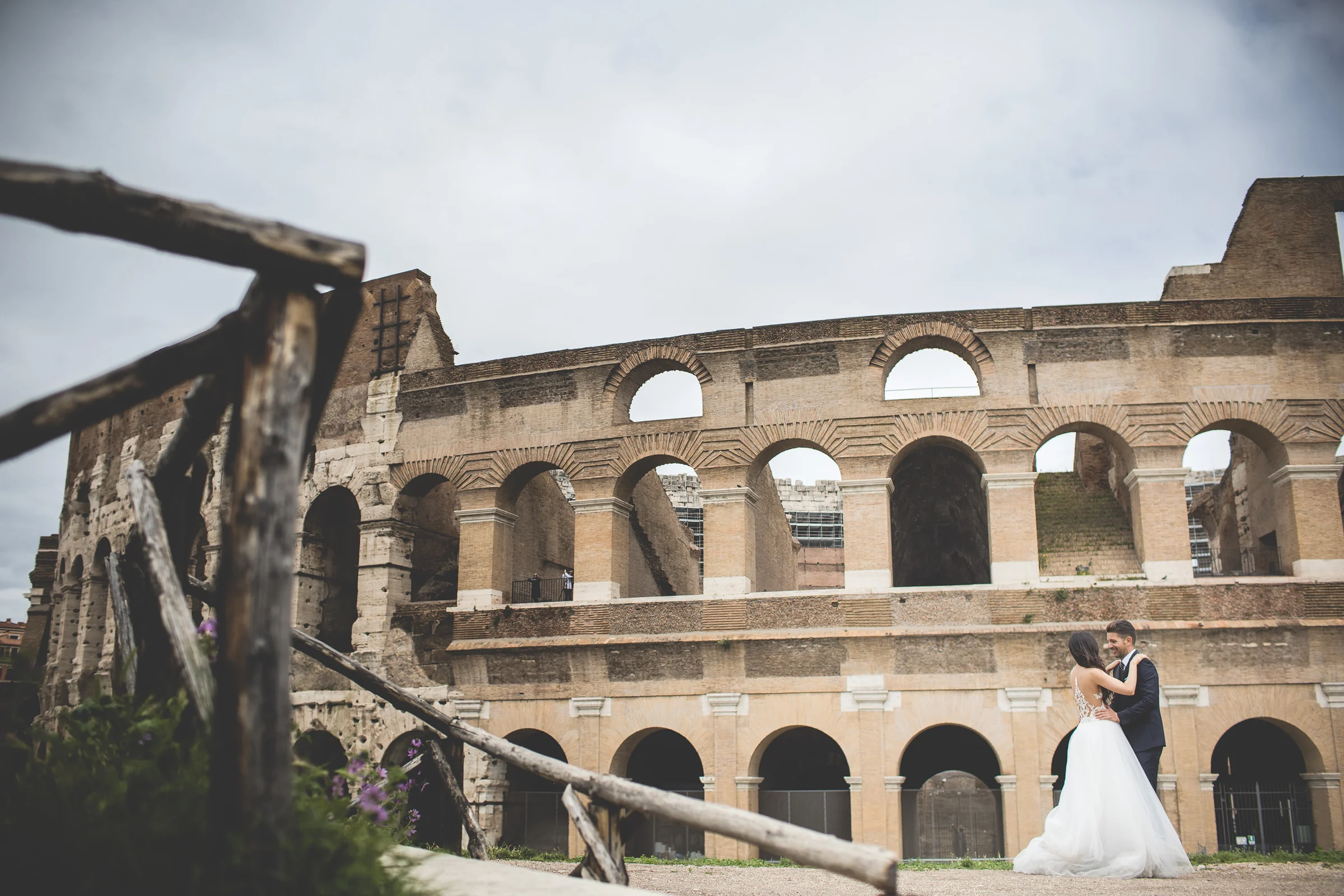 La pareja junto al Coliseo en una composición amplia con arquitectura romana durante una sesión postboda en Coliseo de Roma.