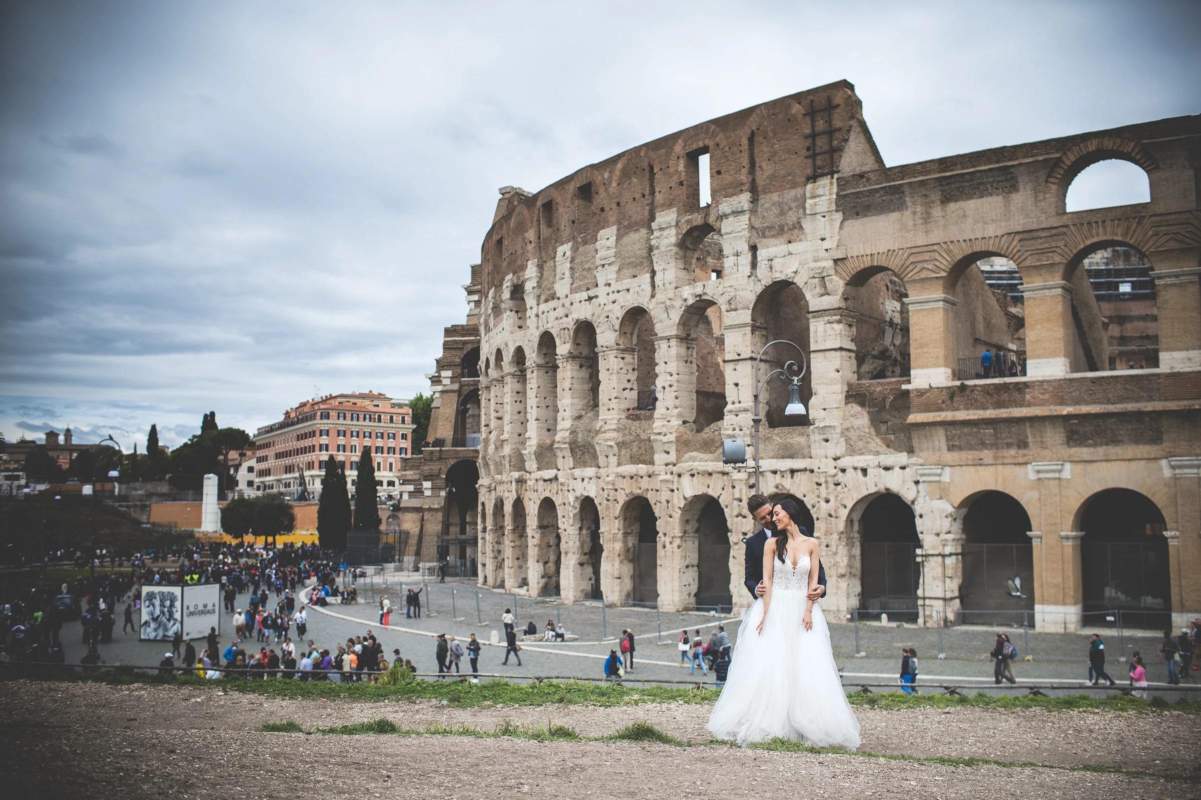 Los novios posan a distancia frente al Coliseo en una vista panorámica durante una sesión postboda en Coliseo de Roma.