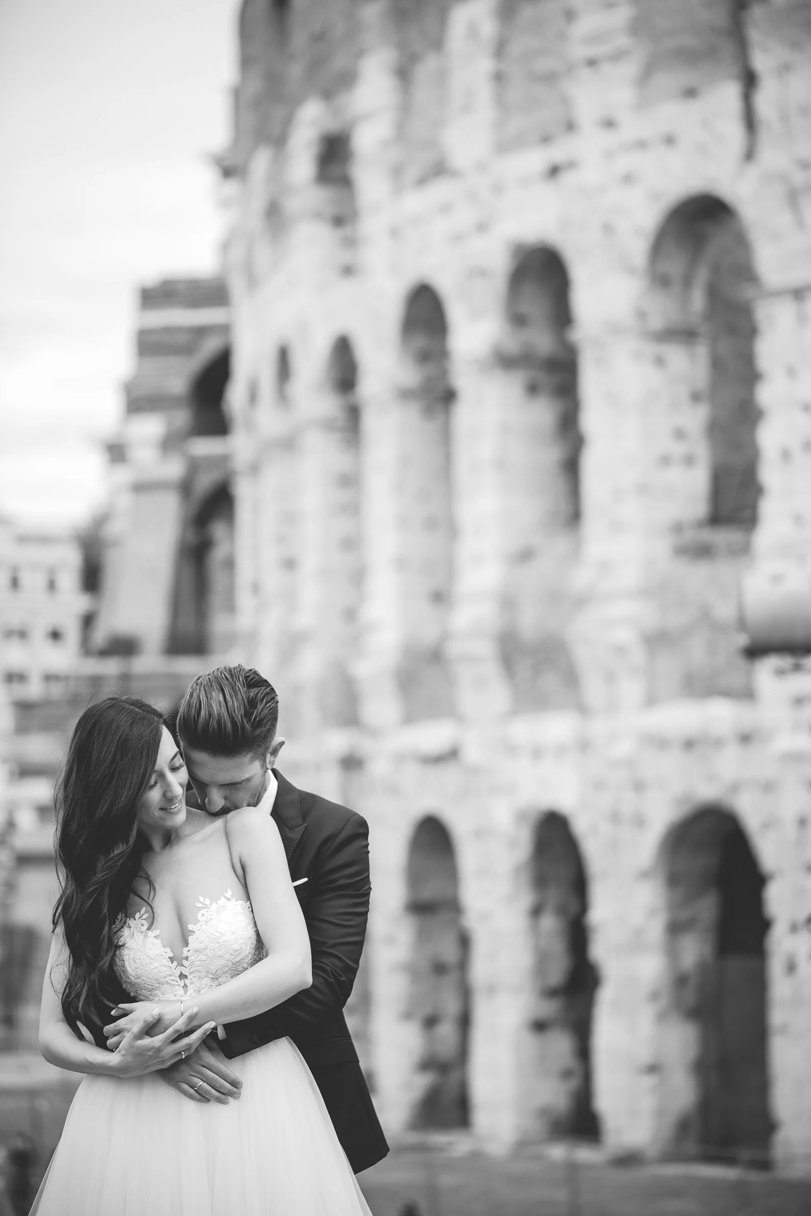 La pareja se abraza en blanco y negro con el Coliseo al fondo durante una sesión postboda en Coliseo de Roma.
