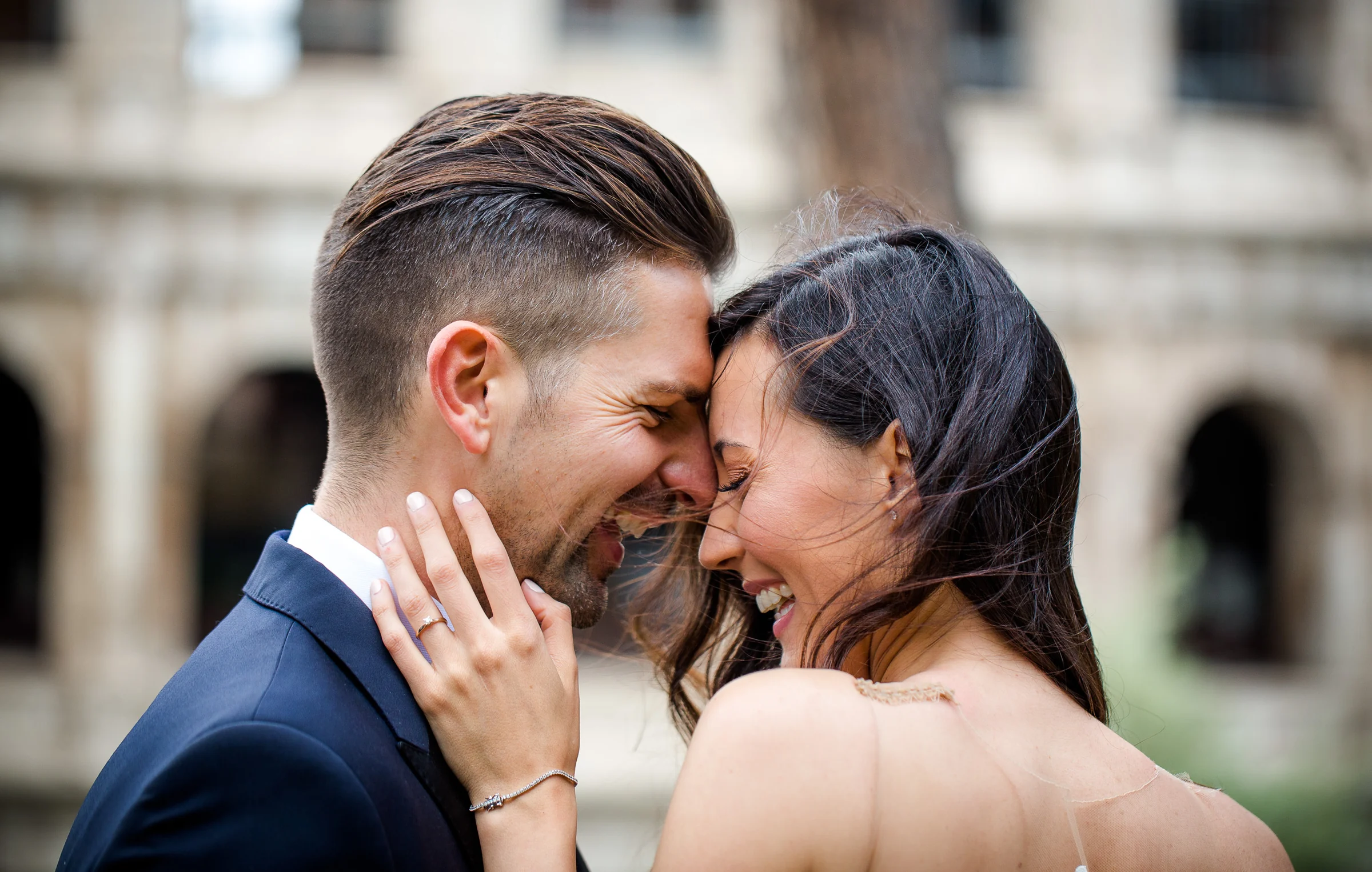 Primer plano de los novios sonriendo y juntando la frente con el Coliseo al fondo durante una sesión postboda en Coliseo de Roma.