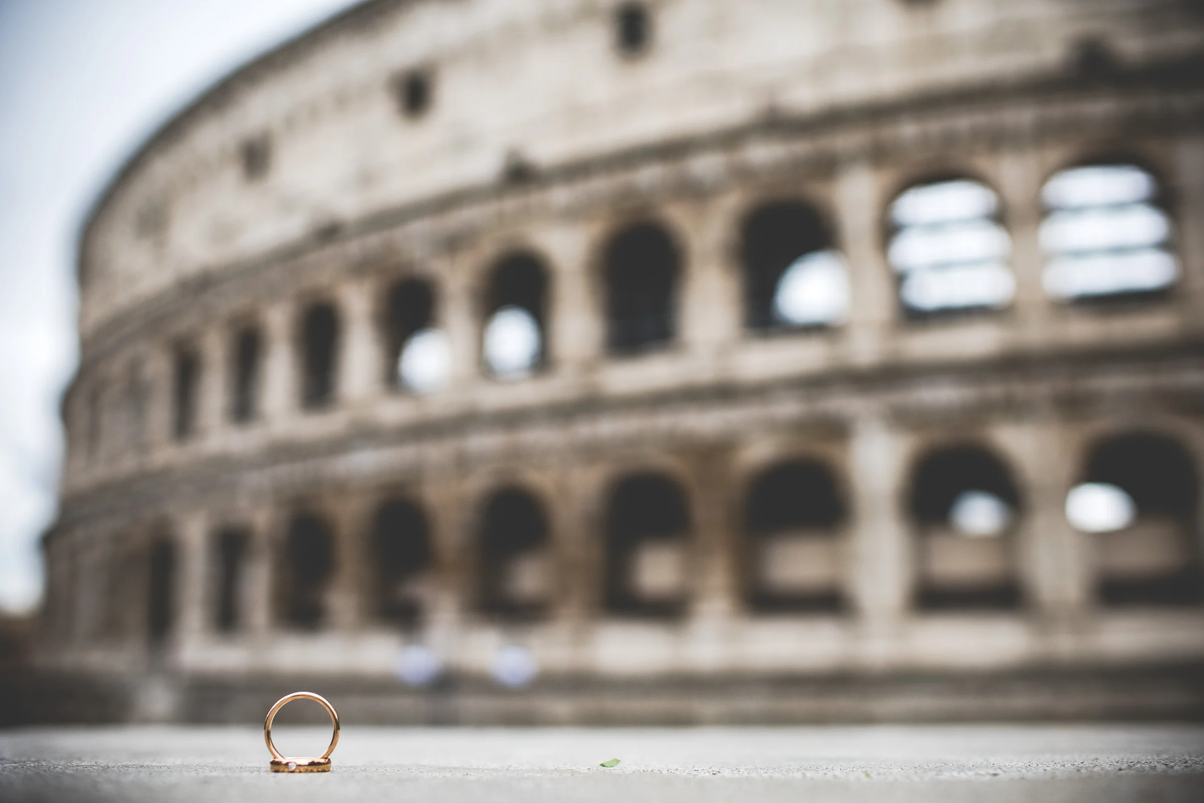 Detalle de las alianzas de boda con el Coliseo desenfocado al fondo durante una sesión postboda en Coliseo de Roma.