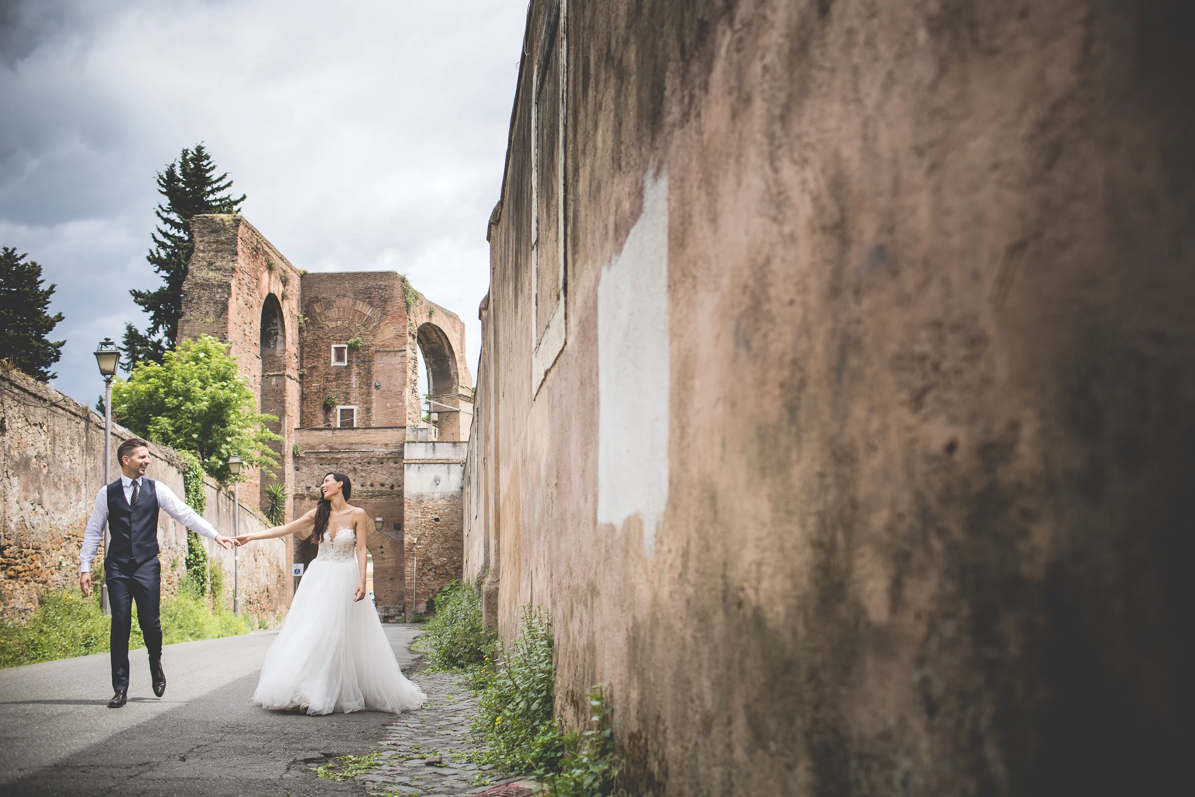La pareja pasea junto a muros históricos del área arqueológica de Roma durante una sesión postboda en Coliseo de Roma.