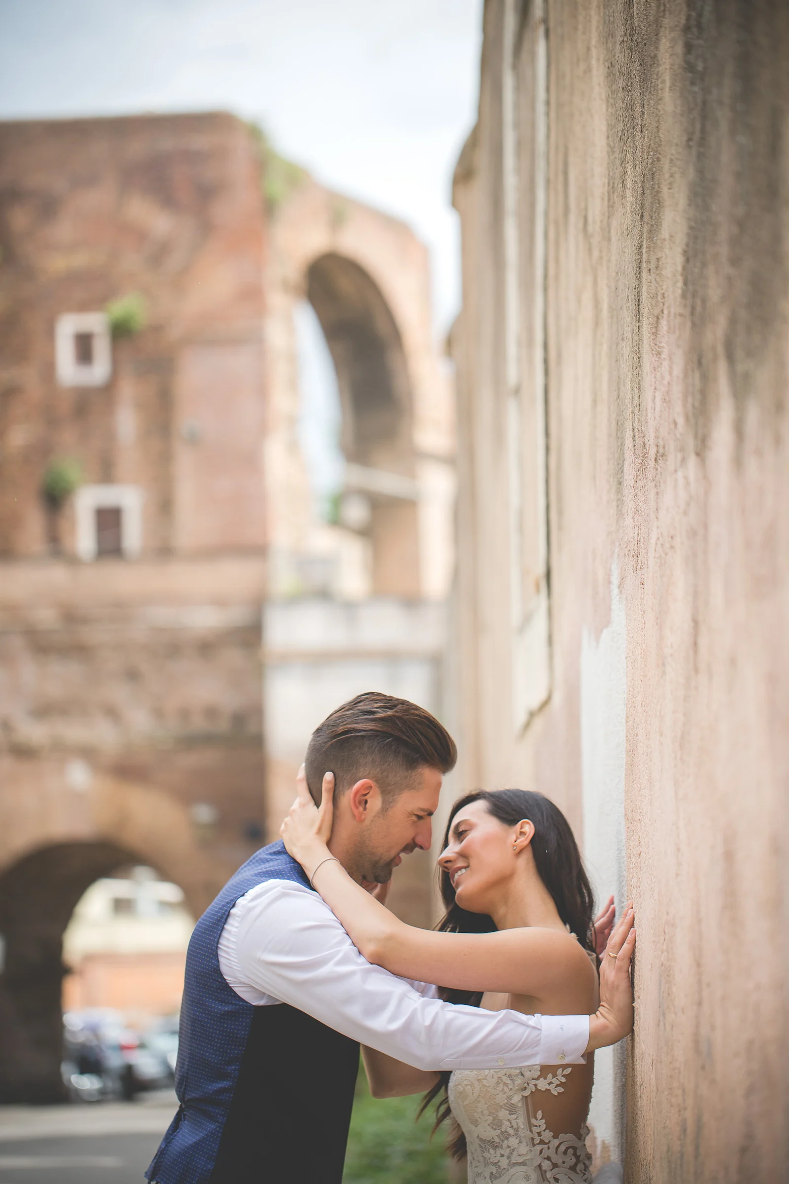 Los novios se besan junto a un muro antiguo con ruinas romanas al fondo durante una sesión postboda en Coliseo de Roma.