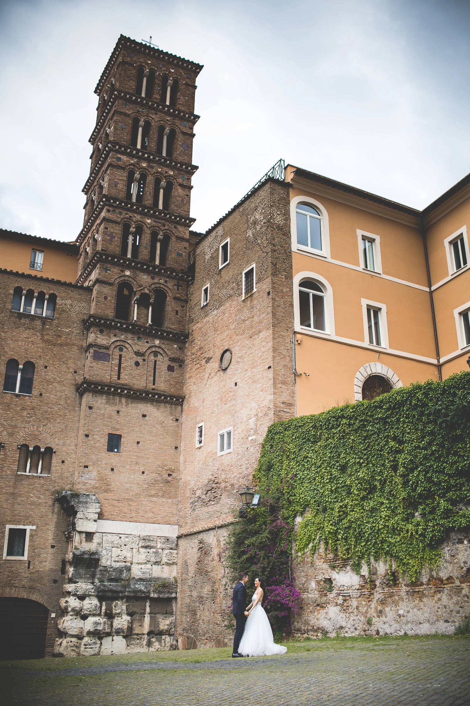 Vista vertical de la pareja integrada en una plaza histórica de Roma durante una sesión postboda en Foro Romano y área arqueológica.