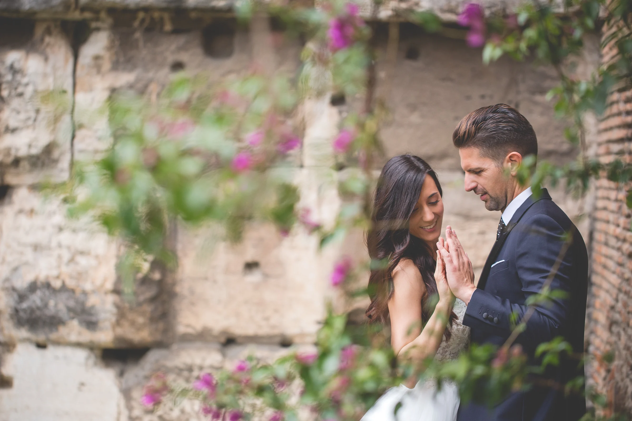 Los novios conversan entre flores y vegetación en un rincón del centro de Roma durante una sesión postboda en Foro Romano y área arqueológica.