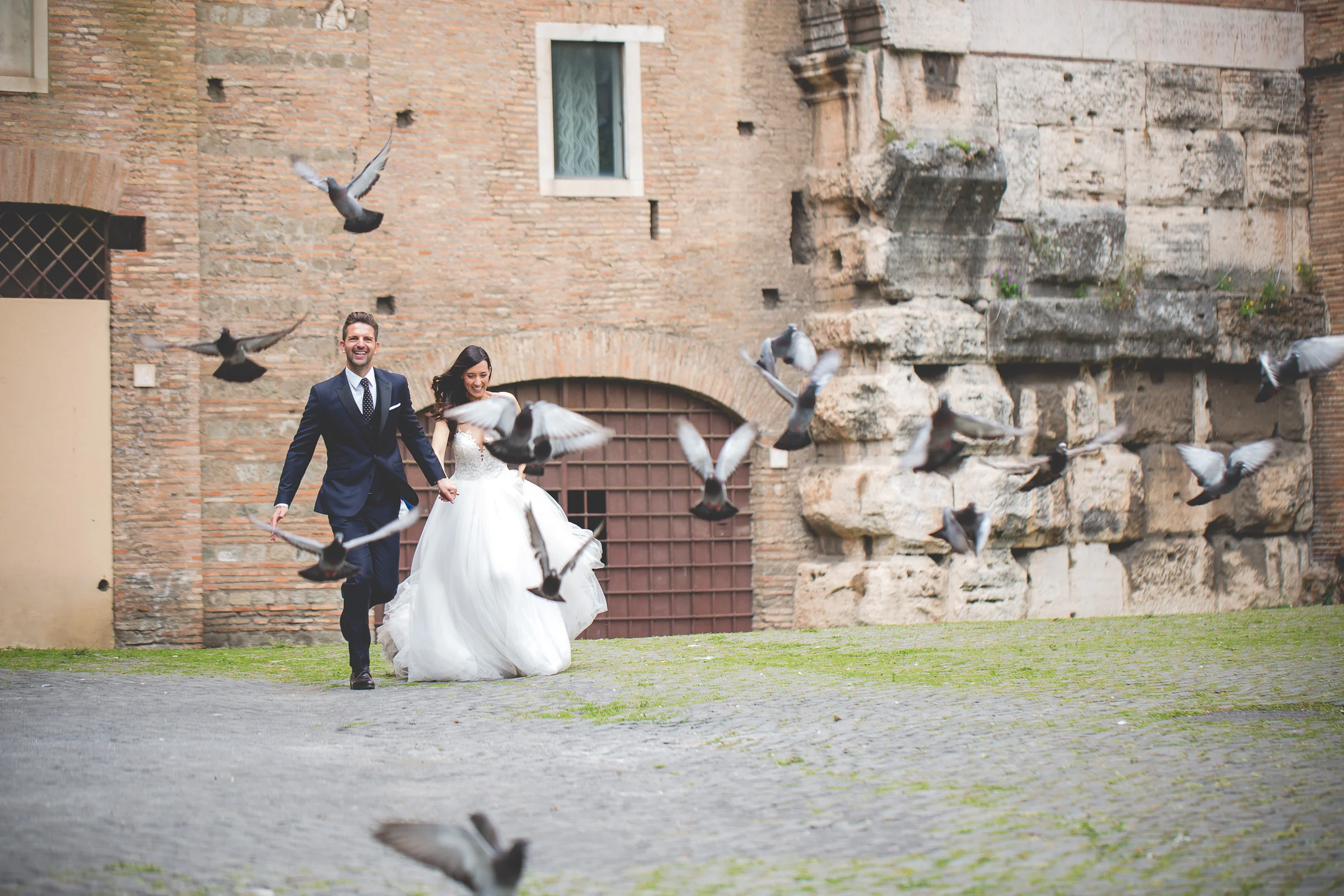 La pareja juega en una plaza de piedra junto a restos arqueológicos durante una sesión postboda en Foro Romano y área arqueológica.