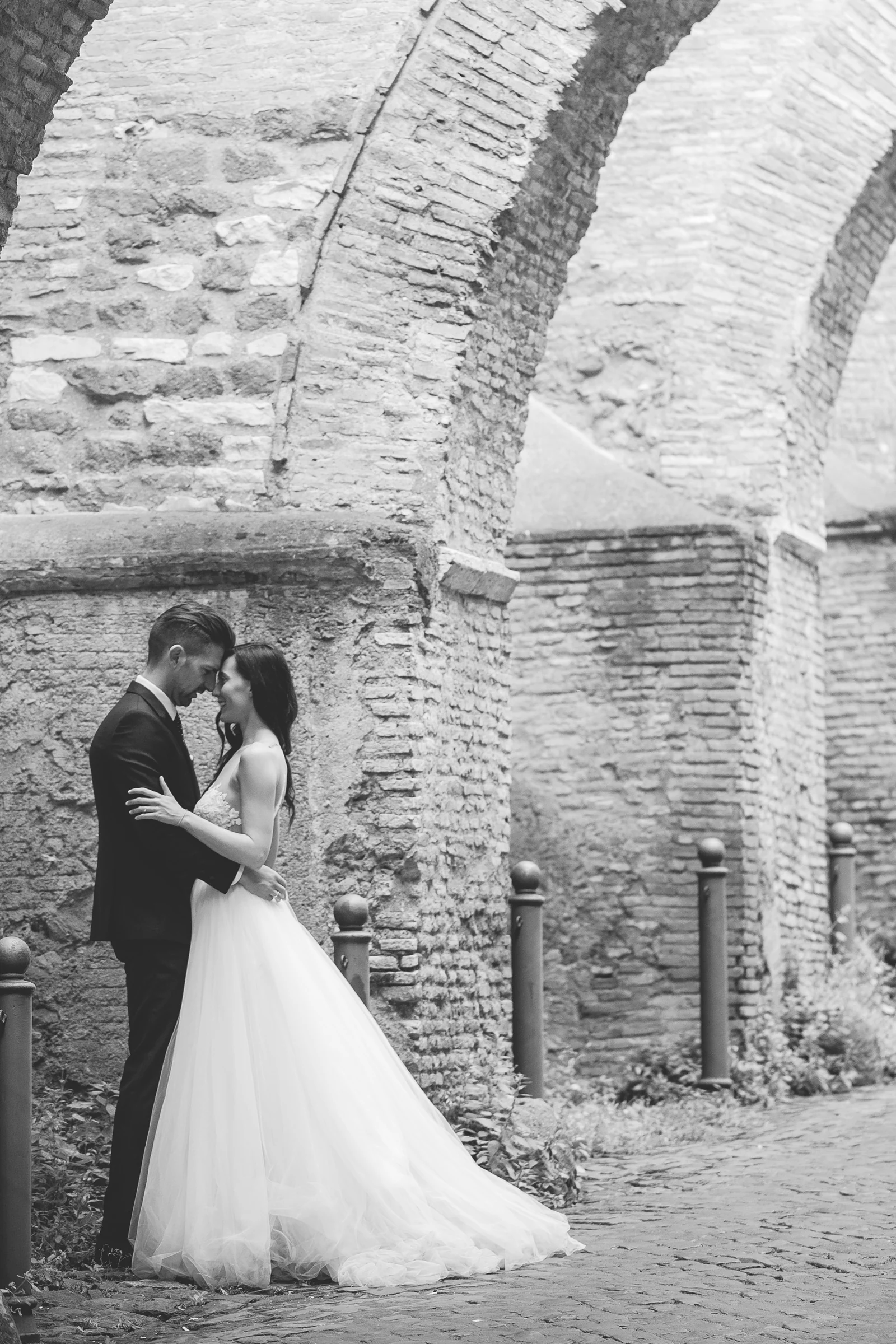 Retrato en blanco y negro de la pareja entre arcos históricos durante una sesión postboda en Foro Romano y área arqueológica.