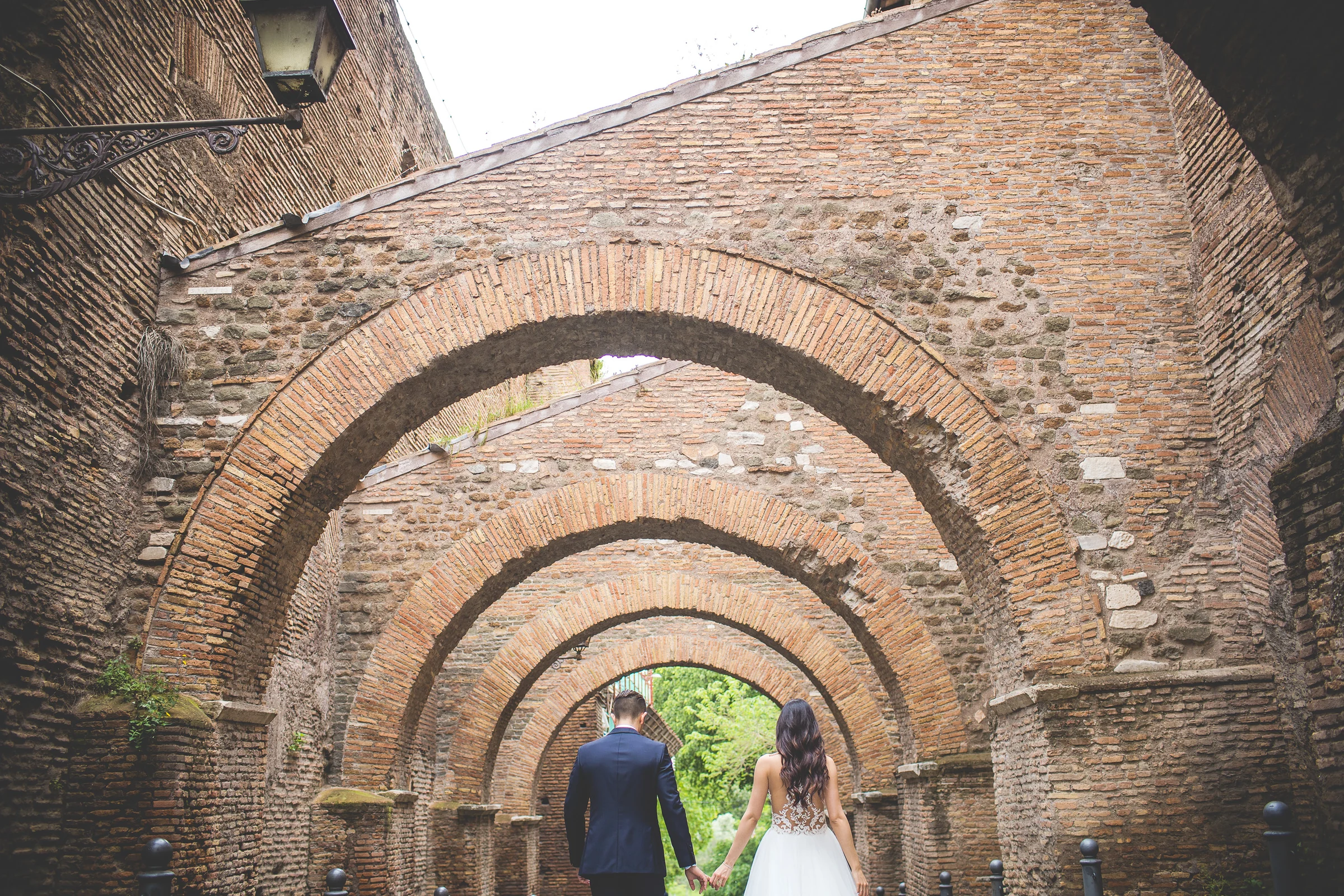 Los novios aparecen al fondo de una composición geométrica bajo arcos de ladrillo durante una sesión postboda en Foro Romano y área arqueológica.