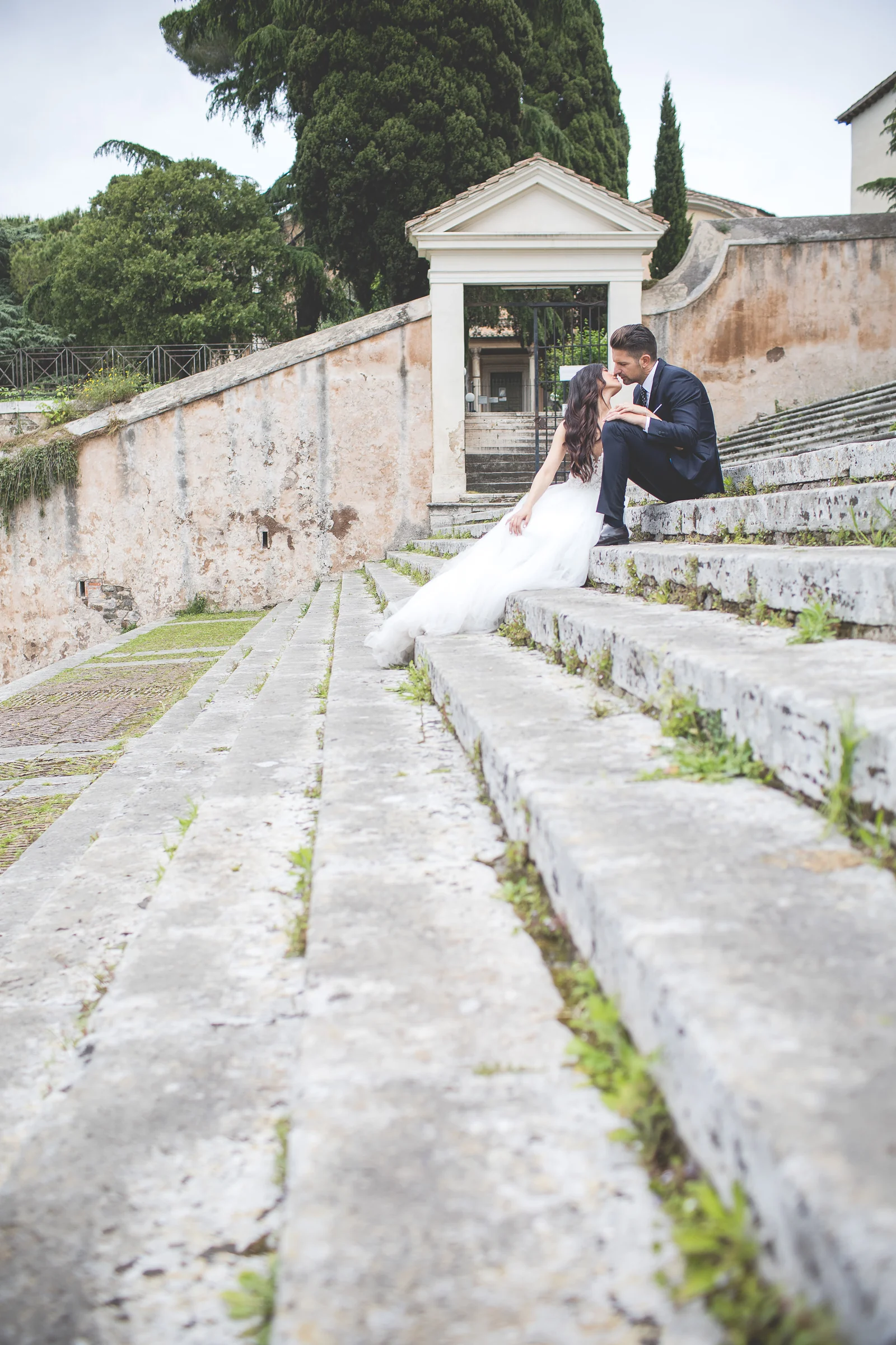 La pareja sentada en una escalinata de piedra dentro del recorrido por Roma durante una sesión postboda en Foro Romano y área arqueológica.