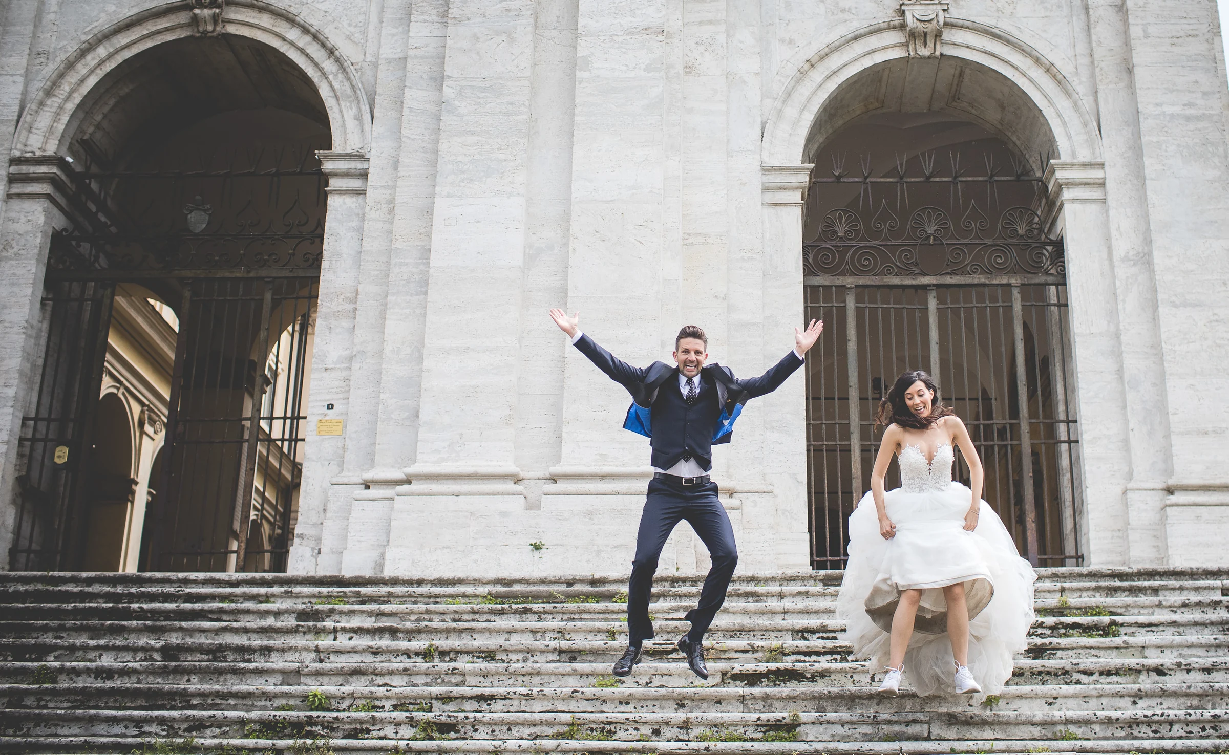 Los novios se divierten en las escaleras de un edificio monumental romano durante una sesión postboda en Foro Romano y área arqueológica.