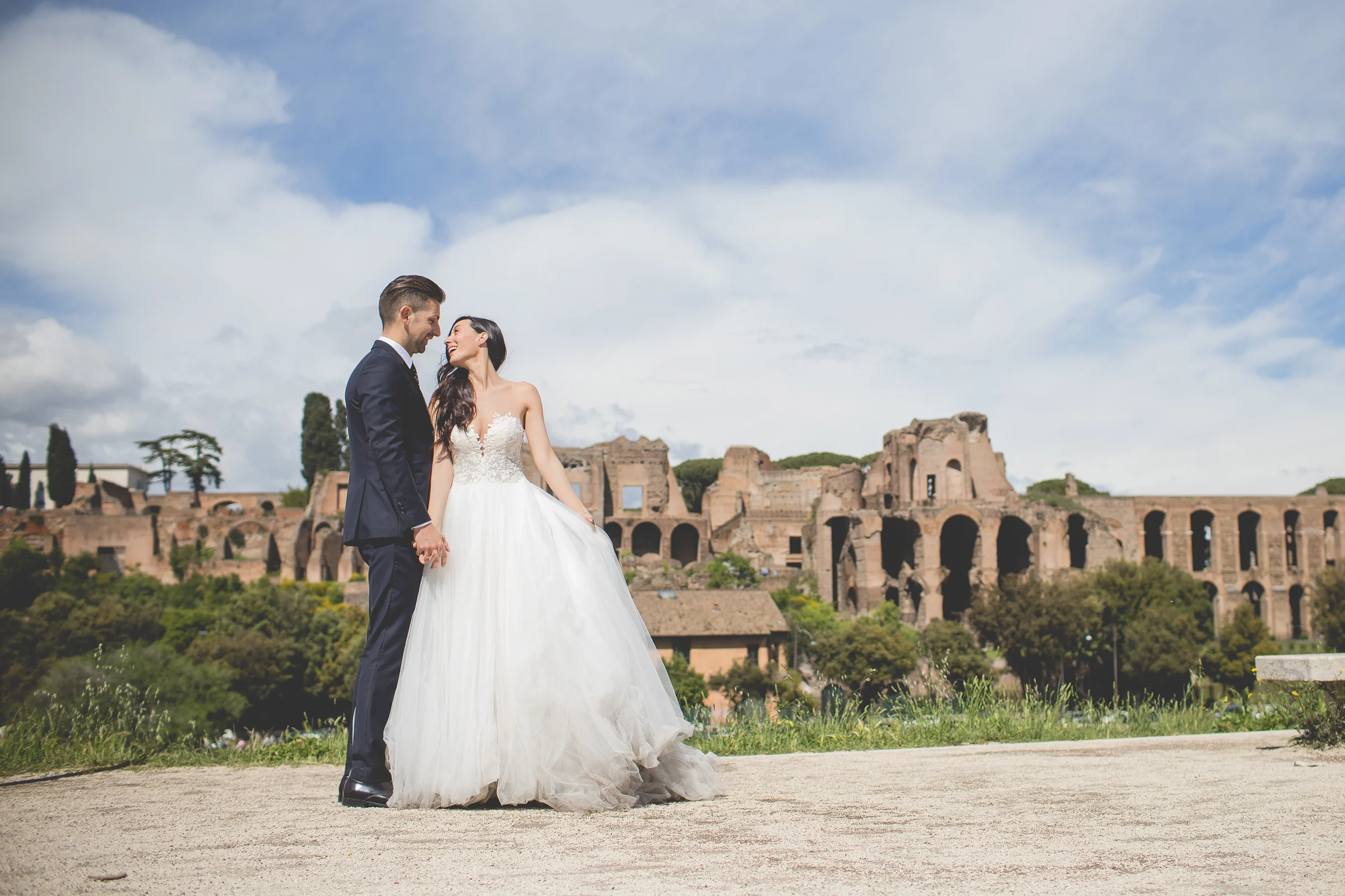 Retrato amplio de la pareja con las ruinas del Foro Romano al fondo durante una sesión postboda en Foro Romano y área arqueológica.