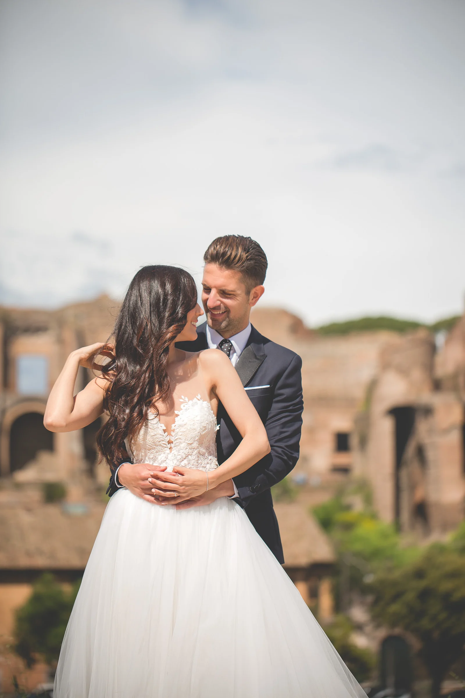 Retrato vertical de los novios abrazados con el Foro Romano de fondo durante una sesión postboda en Foro Romano y área arqueológica.