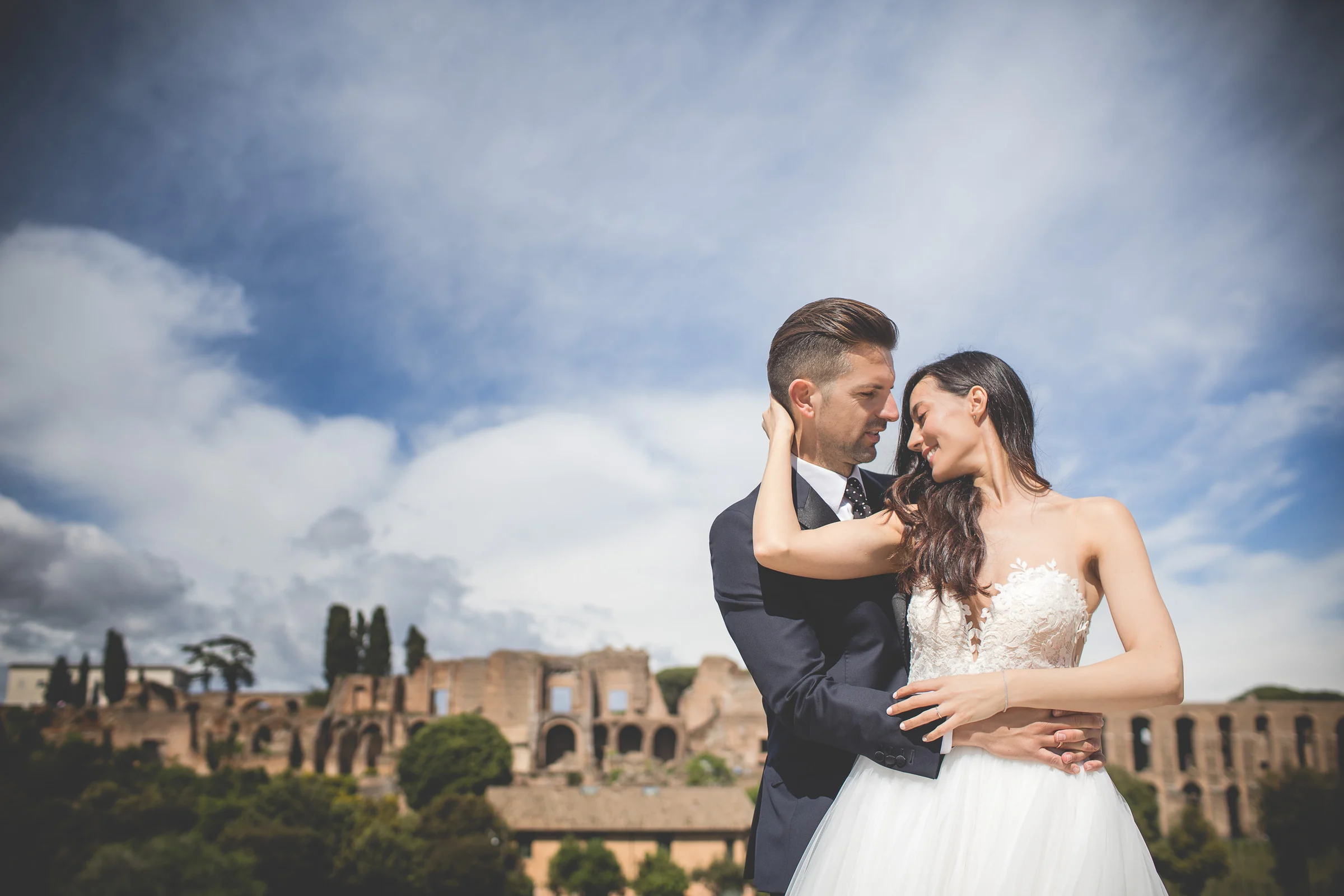 Los novios se abrazan ante una vista panorámica de las ruinas del Foro Romano durante una sesión postboda en Jardines y miradores de Roma.