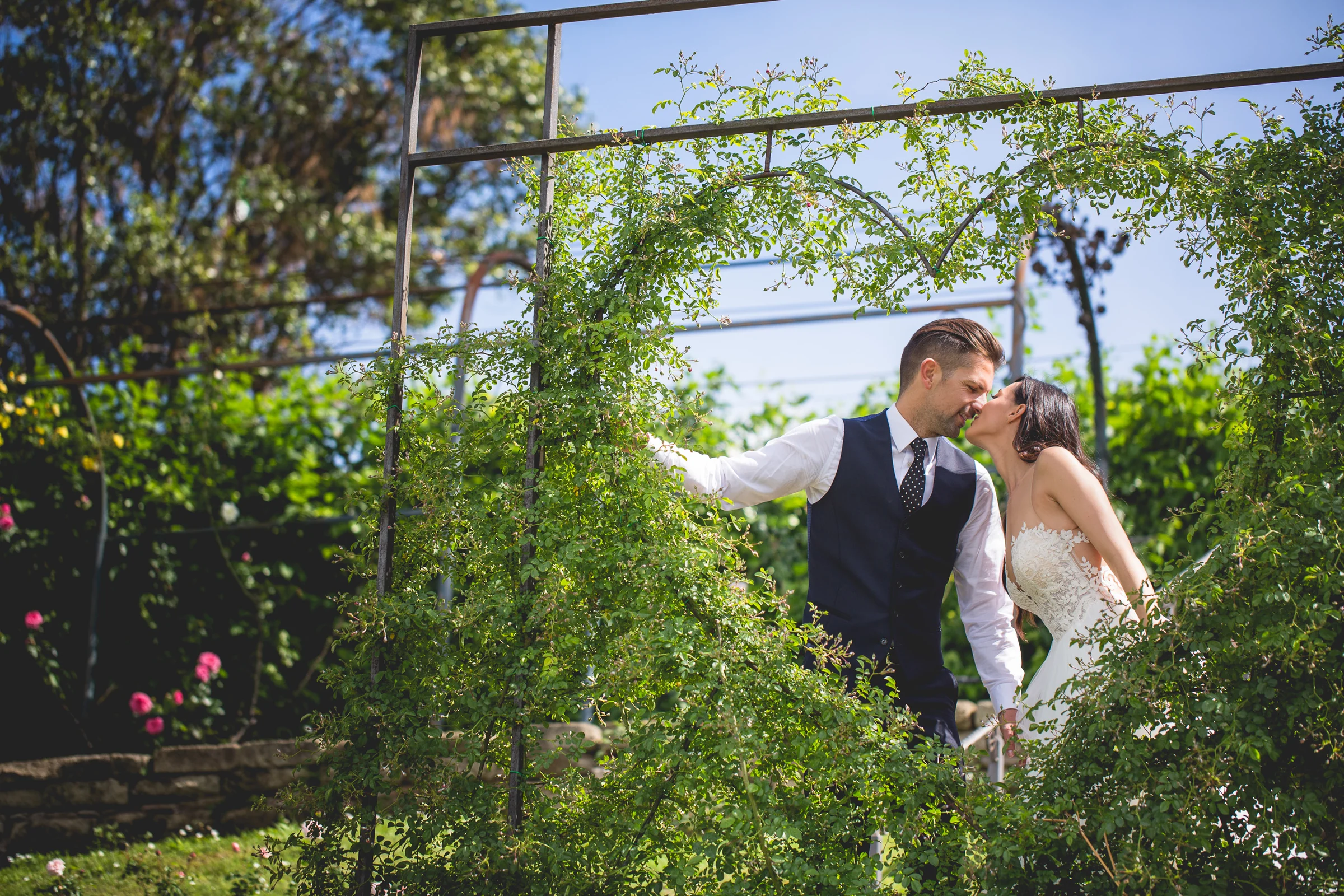 Los novios se besan bajo una estructura vegetal cubierta de rosas durante una sesión postboda en Jardines y miradores de Roma.