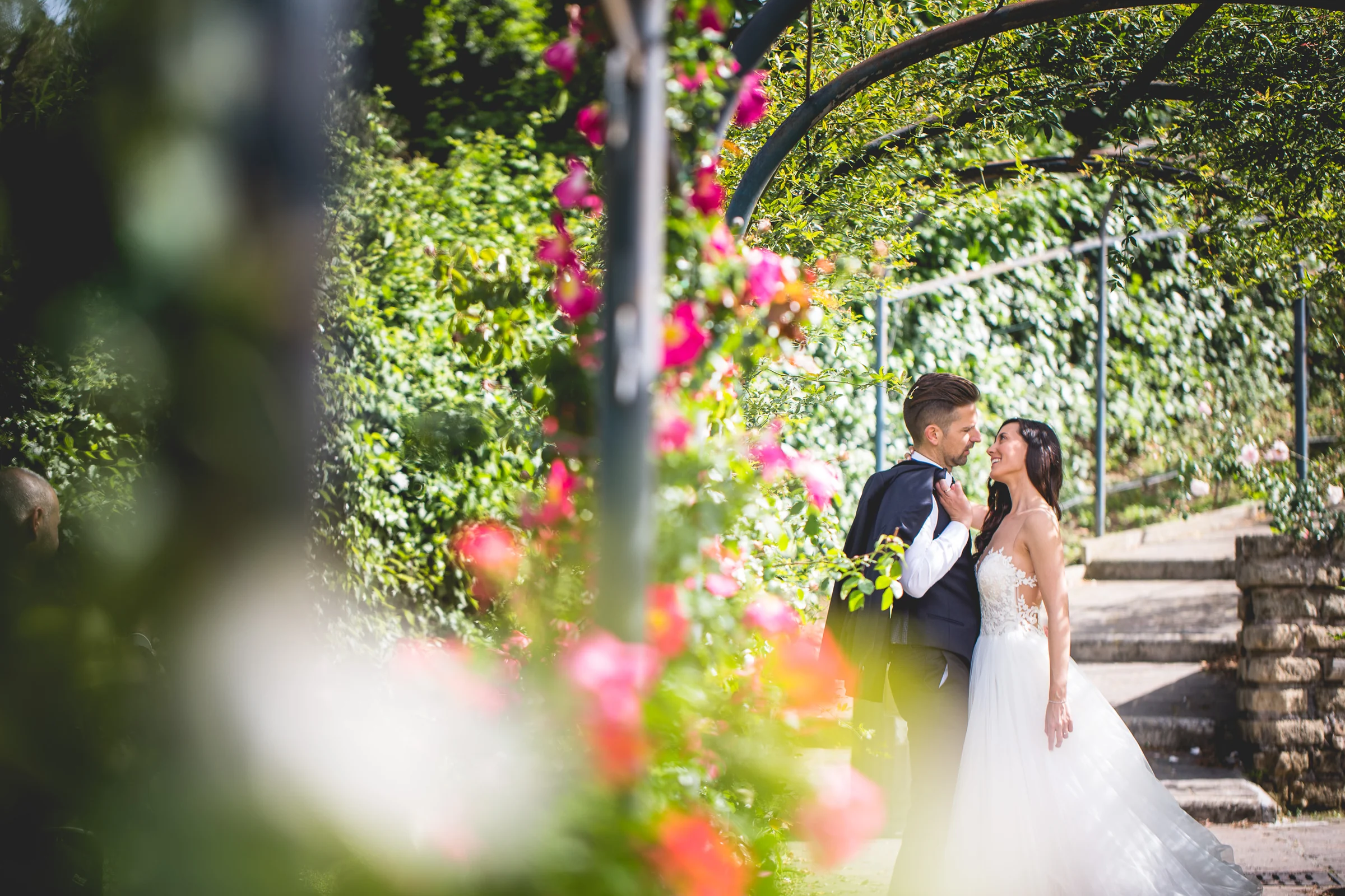 Los novios se abrazan entre rosas y vegetación con un primer plano floral durante una sesión postboda en Jardines y miradores de Roma.