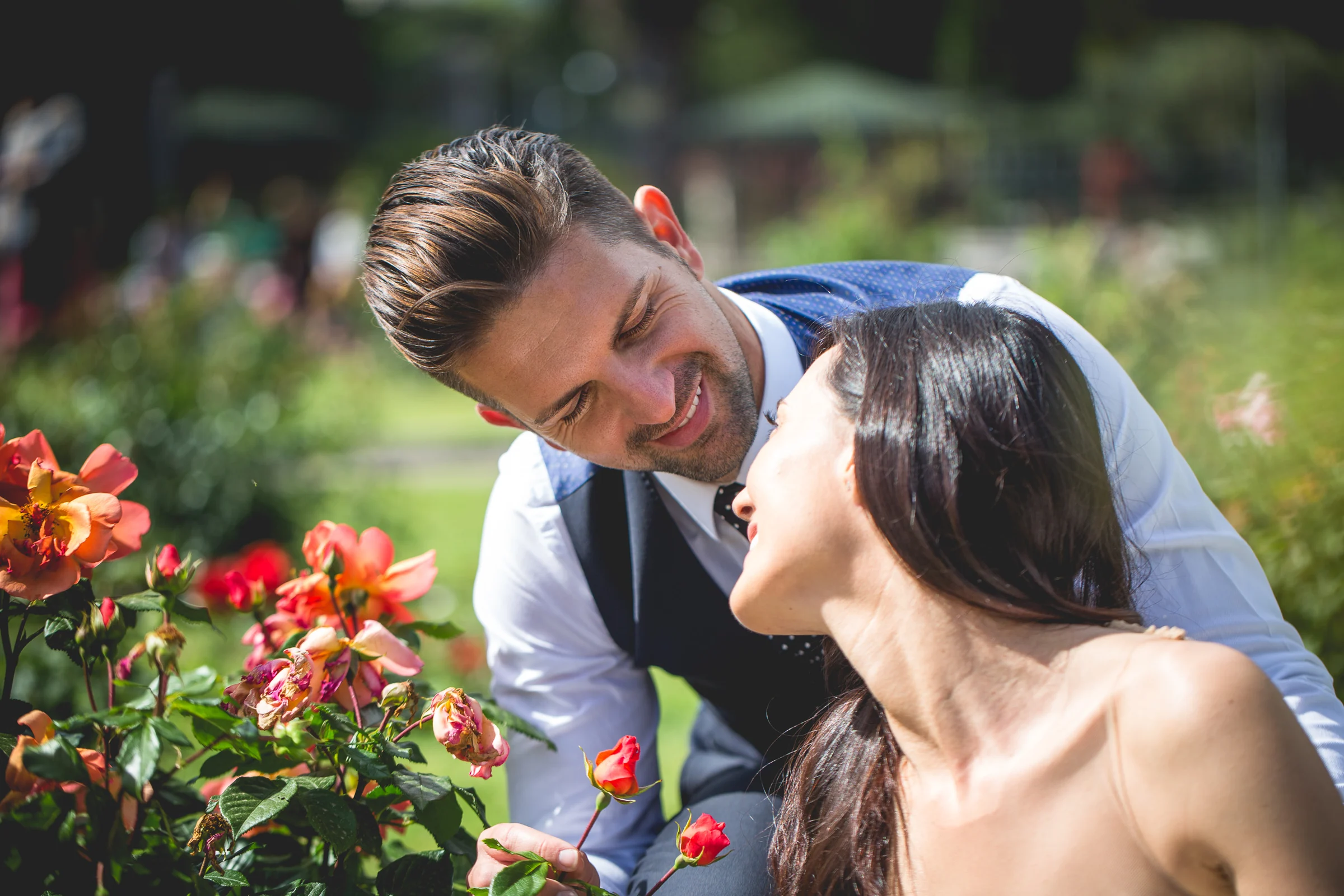 Los novios se acercan entre flores rojas en un retrato romántico durante una sesión postboda en Jardines y miradores de Roma.