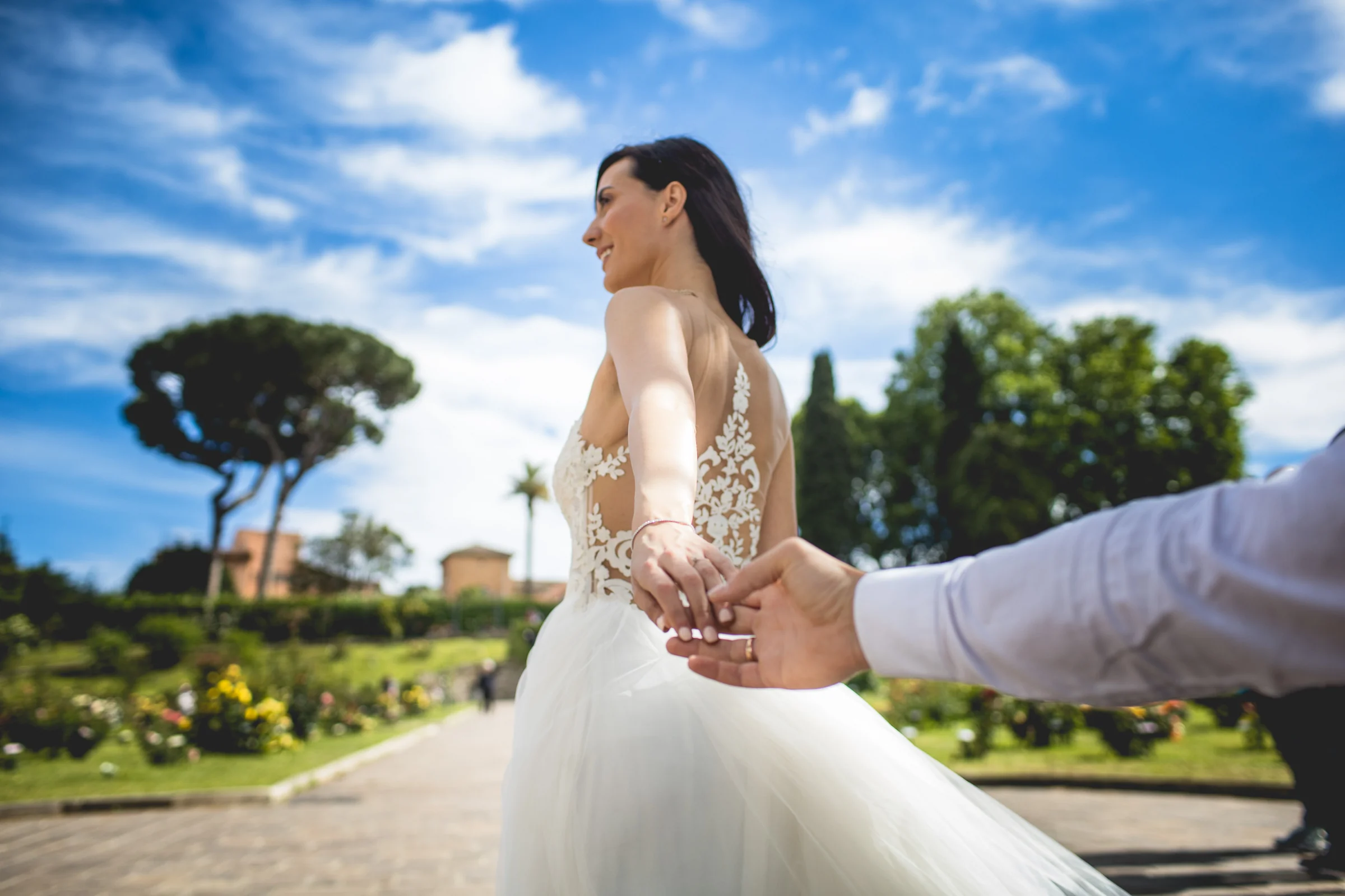 La novia gira con el vestido mientras toma la mano del novio en un jardín durante una sesión postboda en Jardines y miradores de Roma.