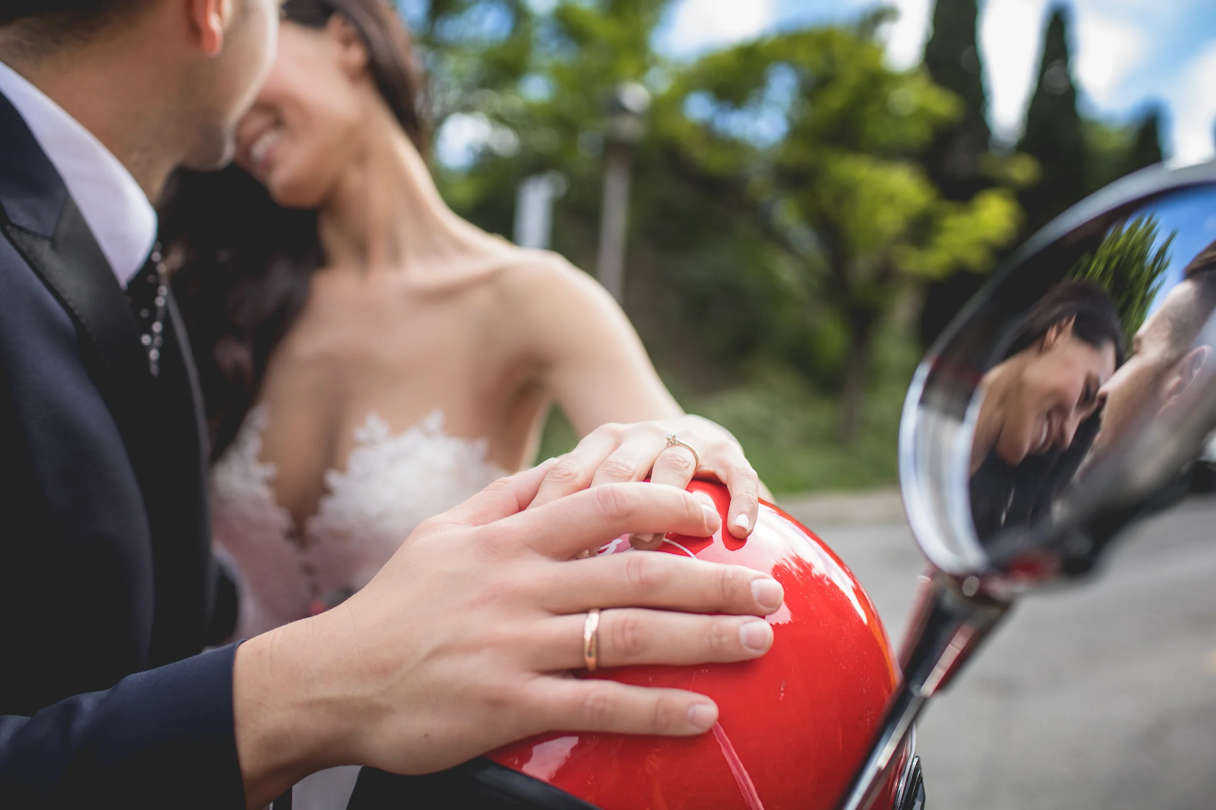 Detalle de las manos y alianzas de los novios sobre una Vespa roja durante una sesión postboda en Calles de Roma con Vespa.