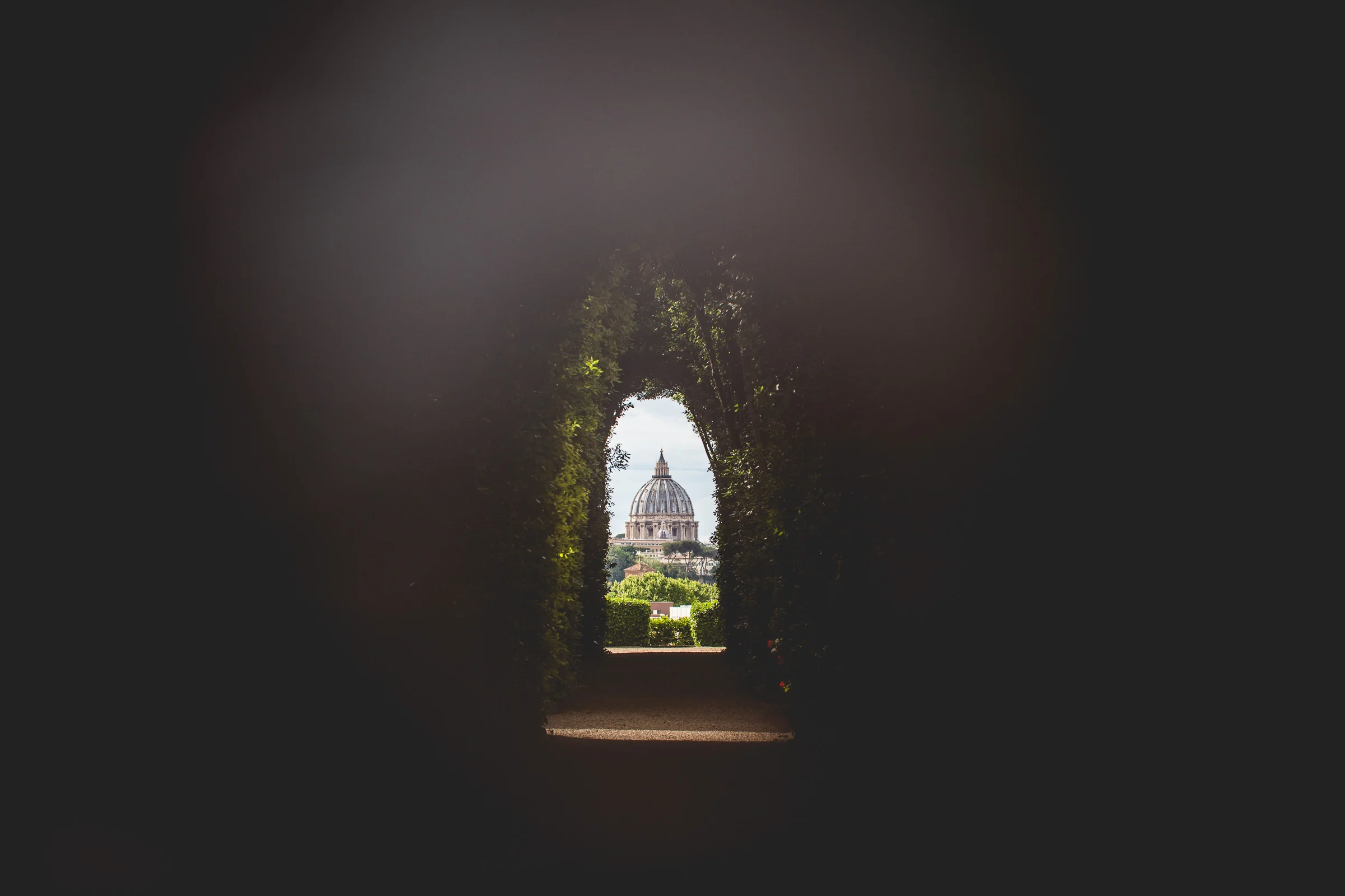 Los novios aparecen enmarcados a través de un arco oscuro con jardín al fondo durante una sesión postboda en Miradores y jardines de Roma.