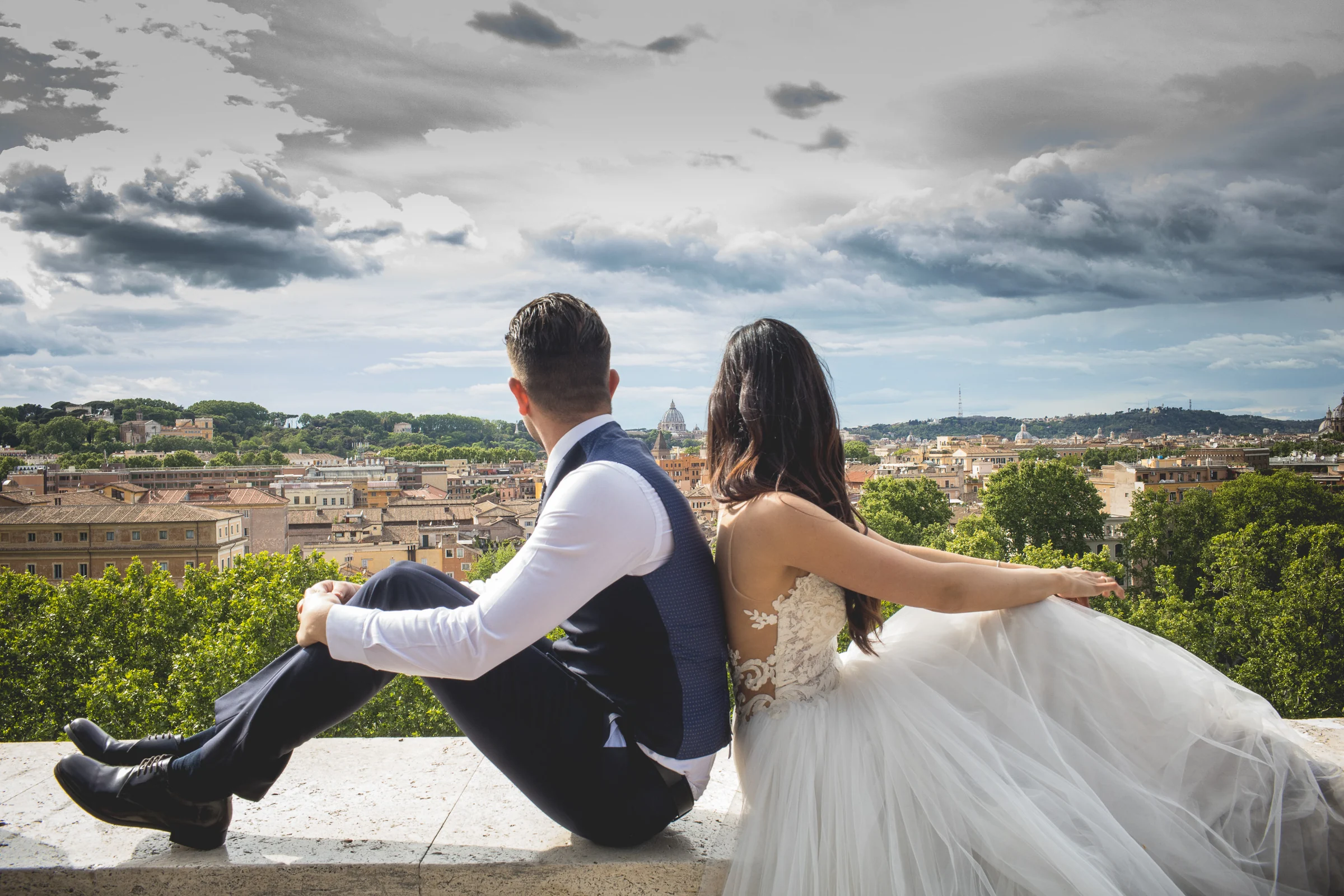 La pareja sentada de espaldas en un mirador con Roma extendiéndose al fondo durante una sesión postboda en Miradores y jardines de Roma.