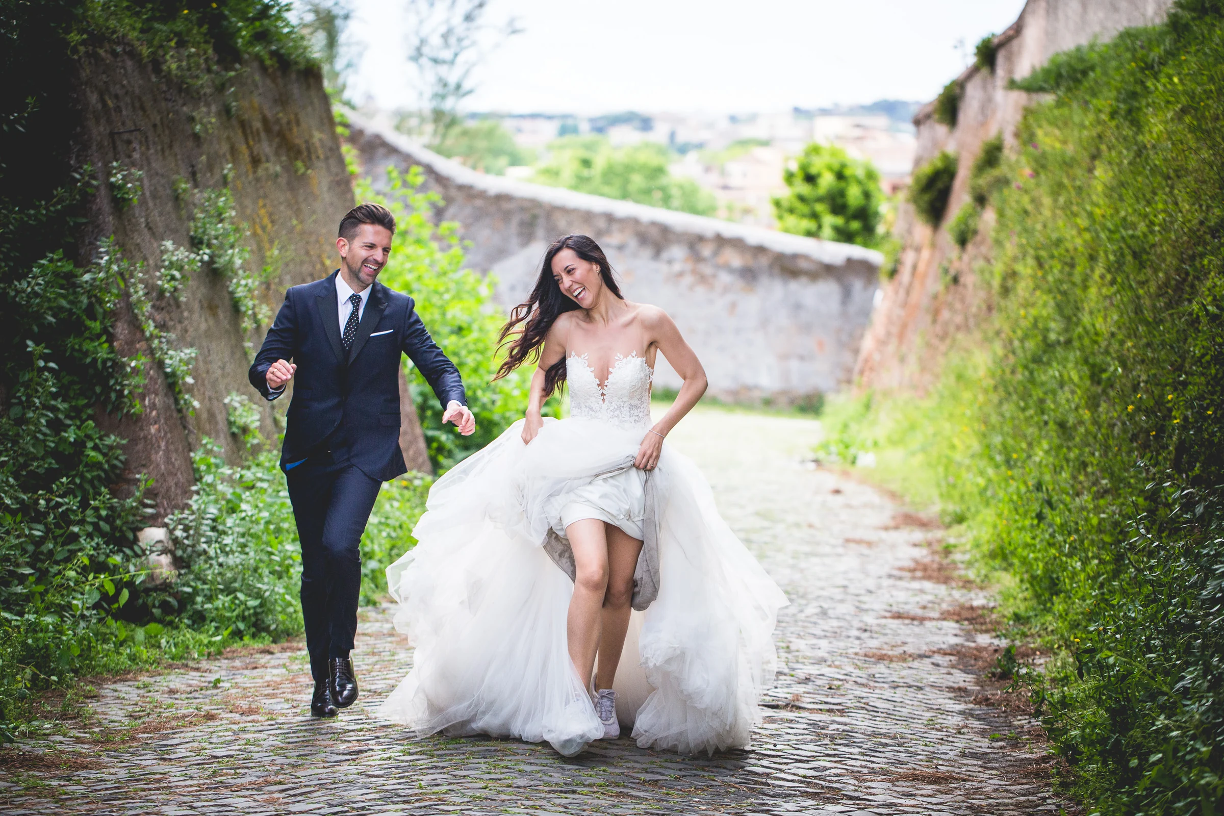 Los novios corren y juegan por un sendero verde de Roma durante una sesión postboda en Miradores y jardines de Roma.