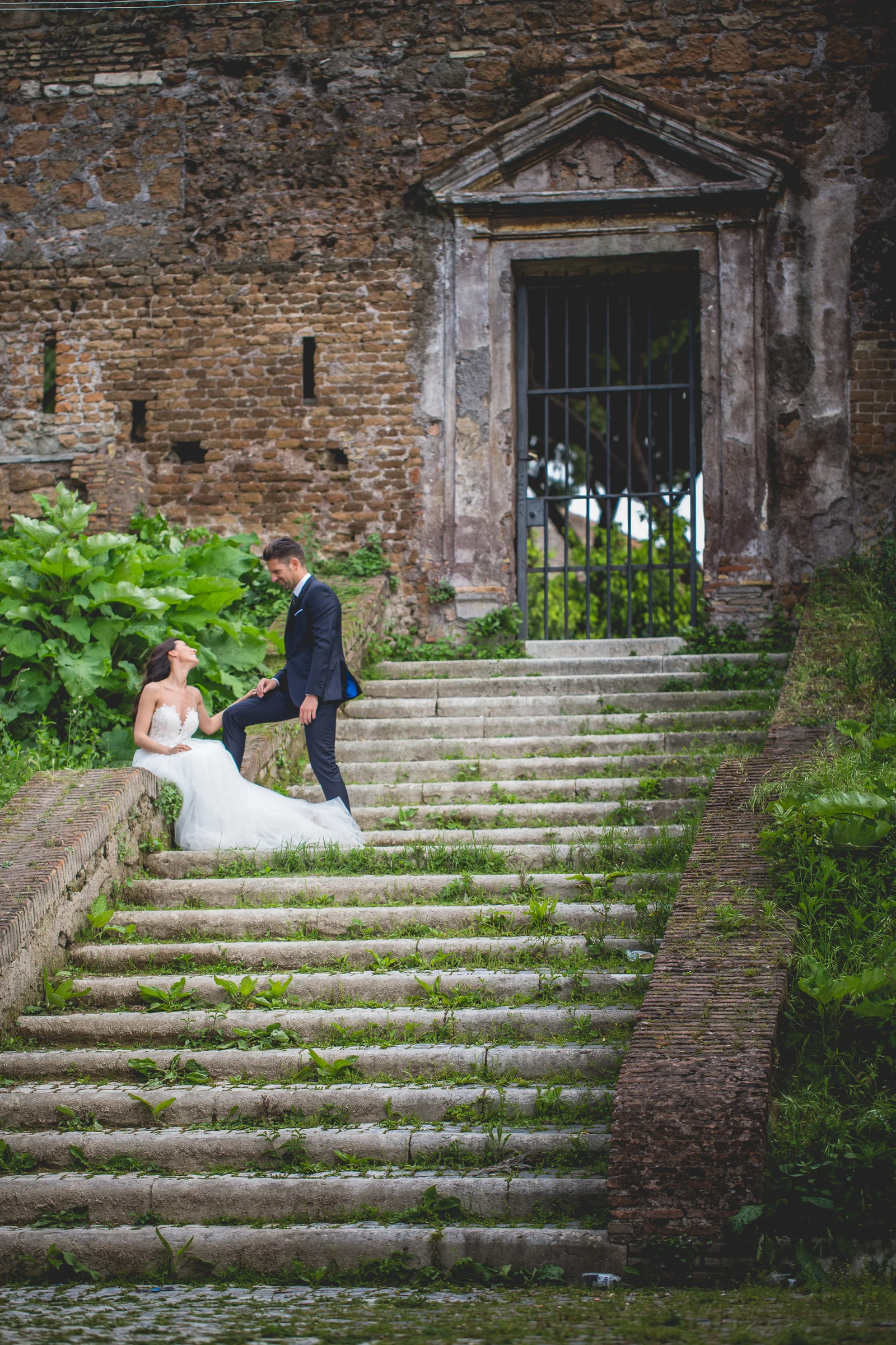La pareja posa en una escalinata de piedra rodeada de vegetación durante una sesión postboda en Miradores y jardines de Roma.
