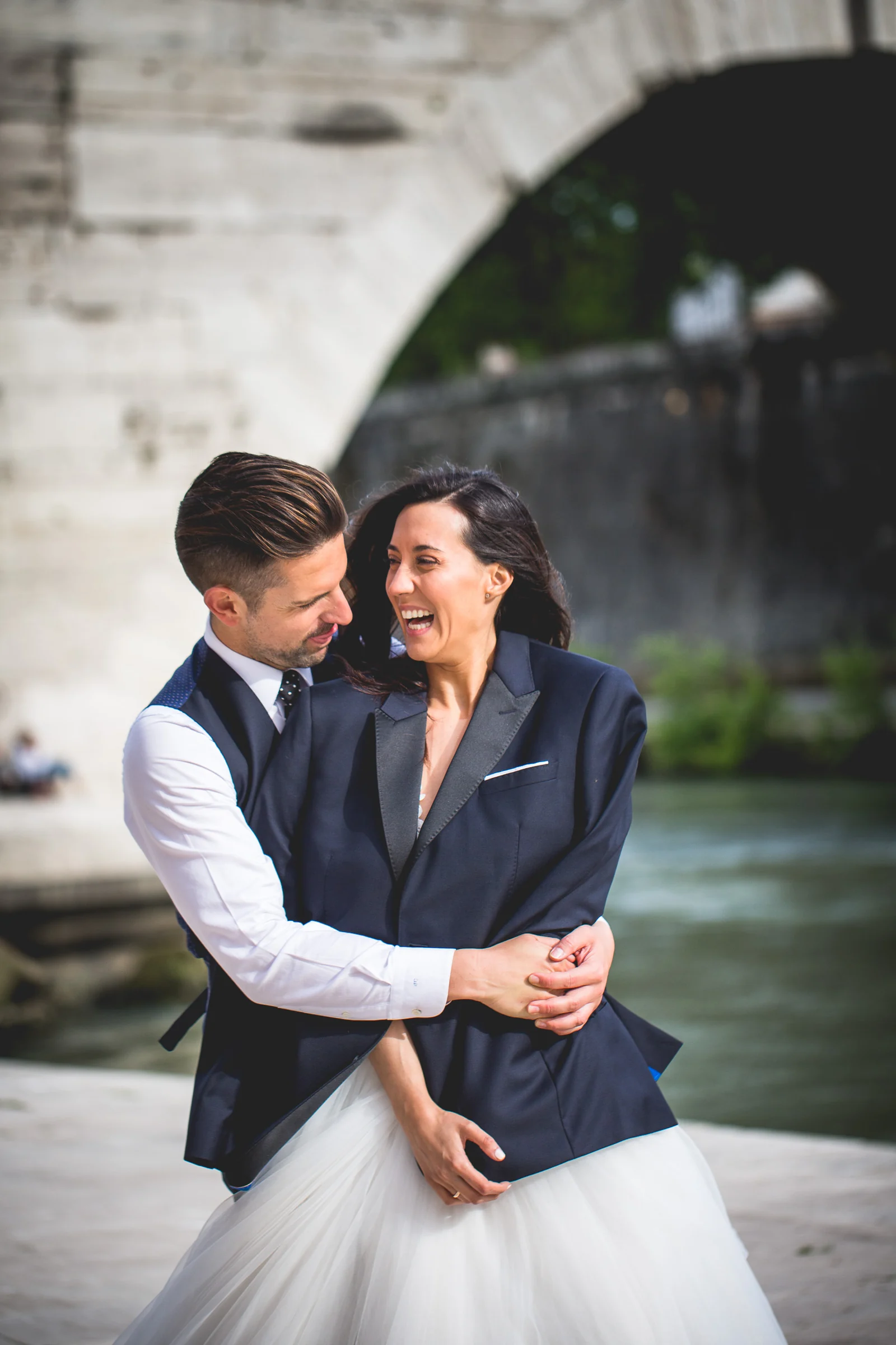 Retrato vertical de la pareja abrazada junto al río Tíber durante una sesión postboda en Río Tíber y puentes de Roma.
