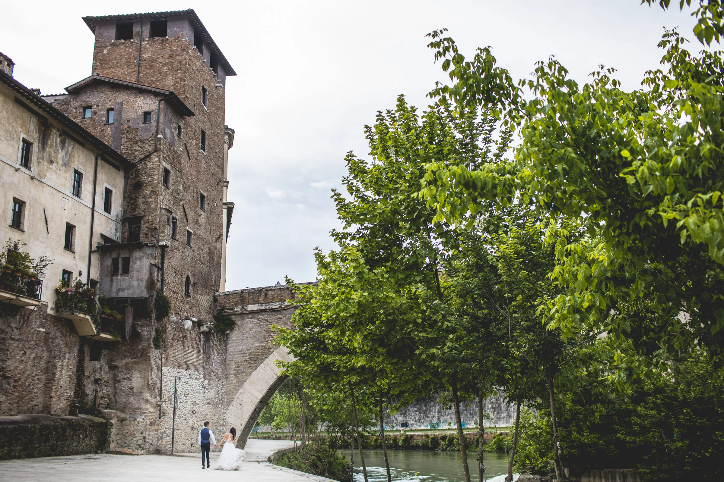 La pareja aparece a distancia junto al Tíber y arquitectura histórica durante una sesión postboda en Río Tíber y puentes de Roma.