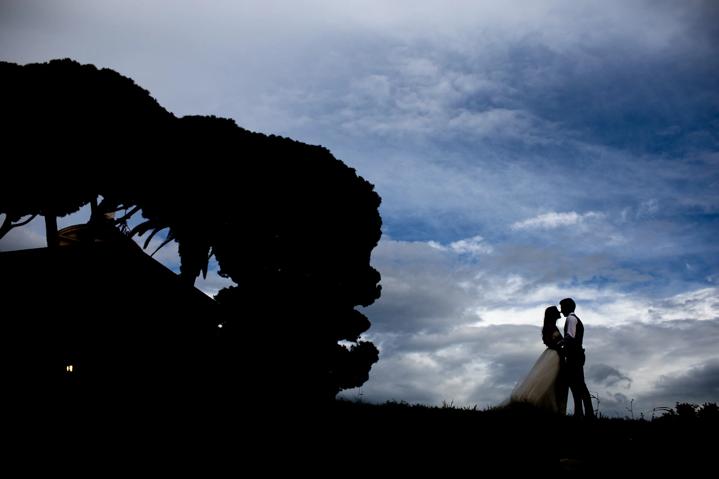 Silueta de la pareja besándose bajo un cielo dramático junto al Tíber durante una sesión postboda en Río Tíber y puentes de Roma.