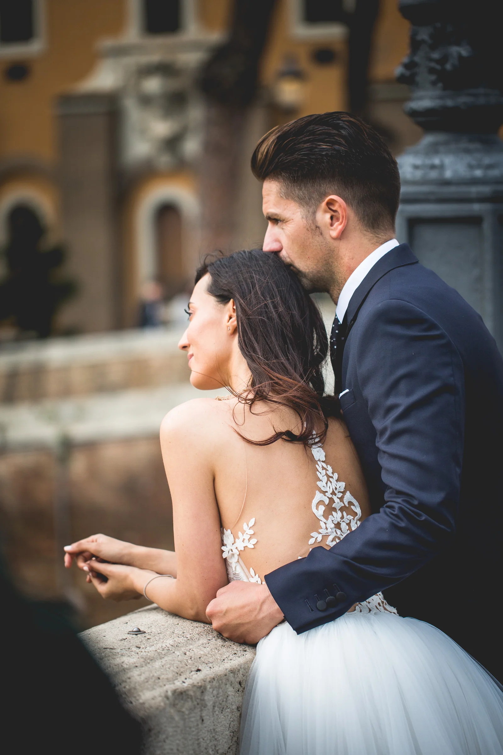 Retrato vertical de los novios abrazados junto a una balaustrada de piedra durante una sesión postboda en Miradores y centro histórico de Roma.