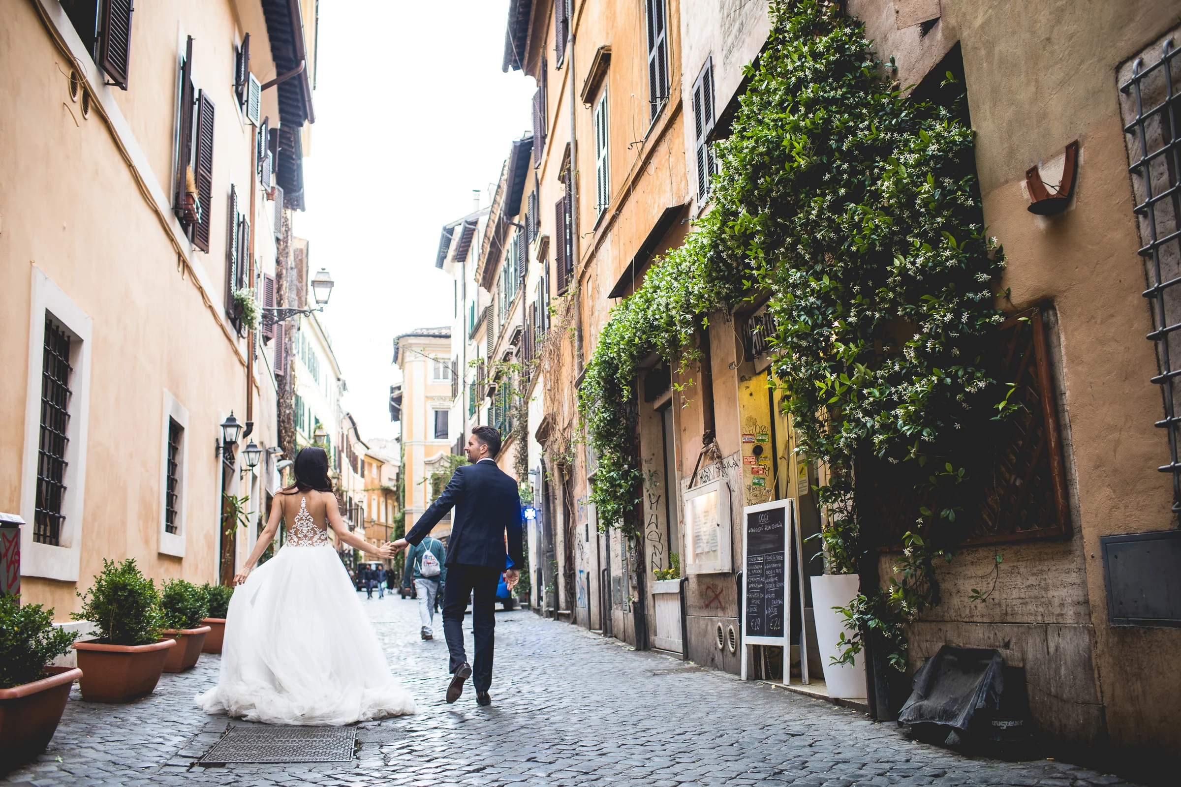 La pareja camina de la mano por una calle estrecha del centro histórico durante una sesión postboda en Miradores y centro histórico de Roma.