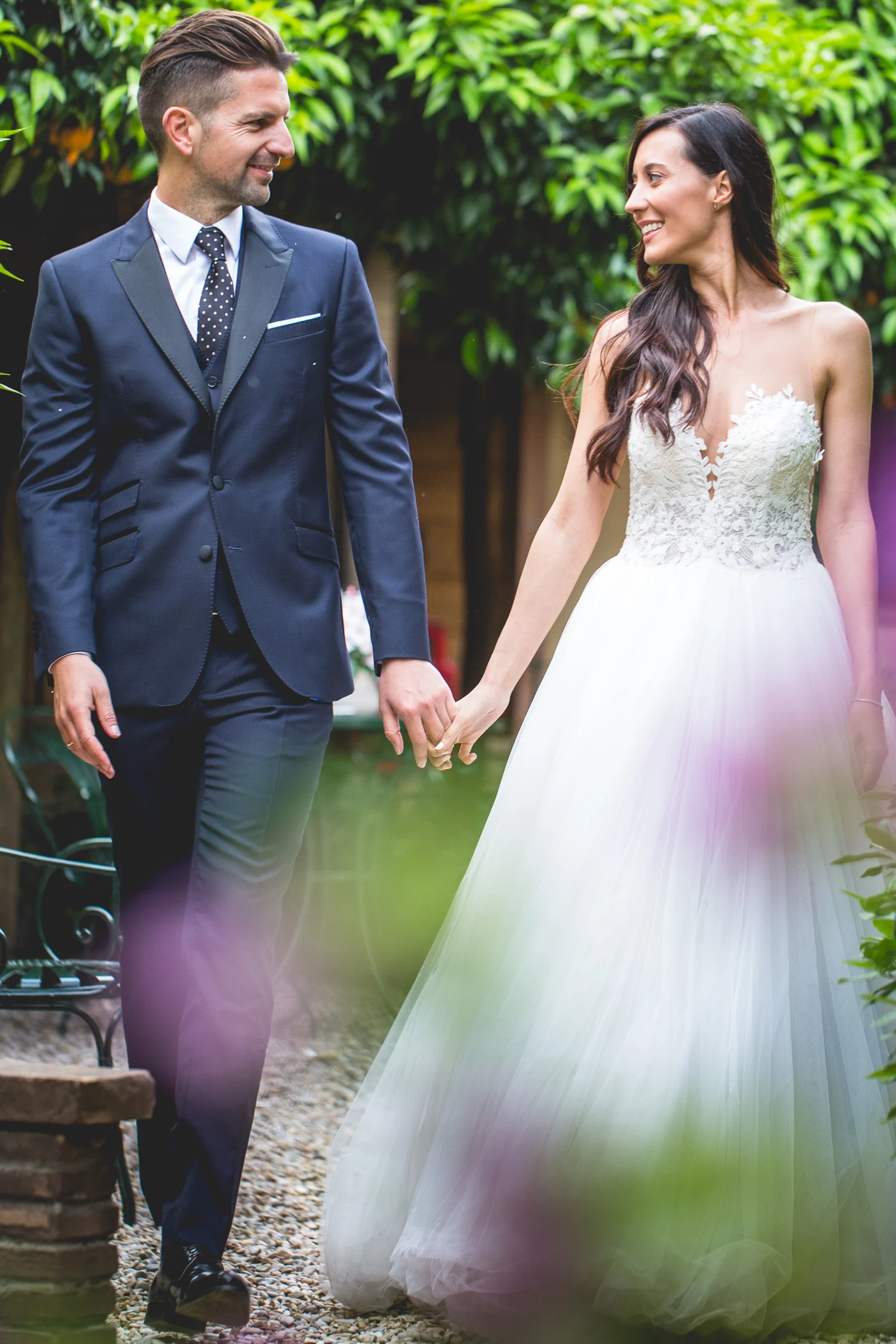 Los novios caminan entre flores y vegetación en una calle de Roma durante una sesión postboda en Miradores y centro histórico de Roma.