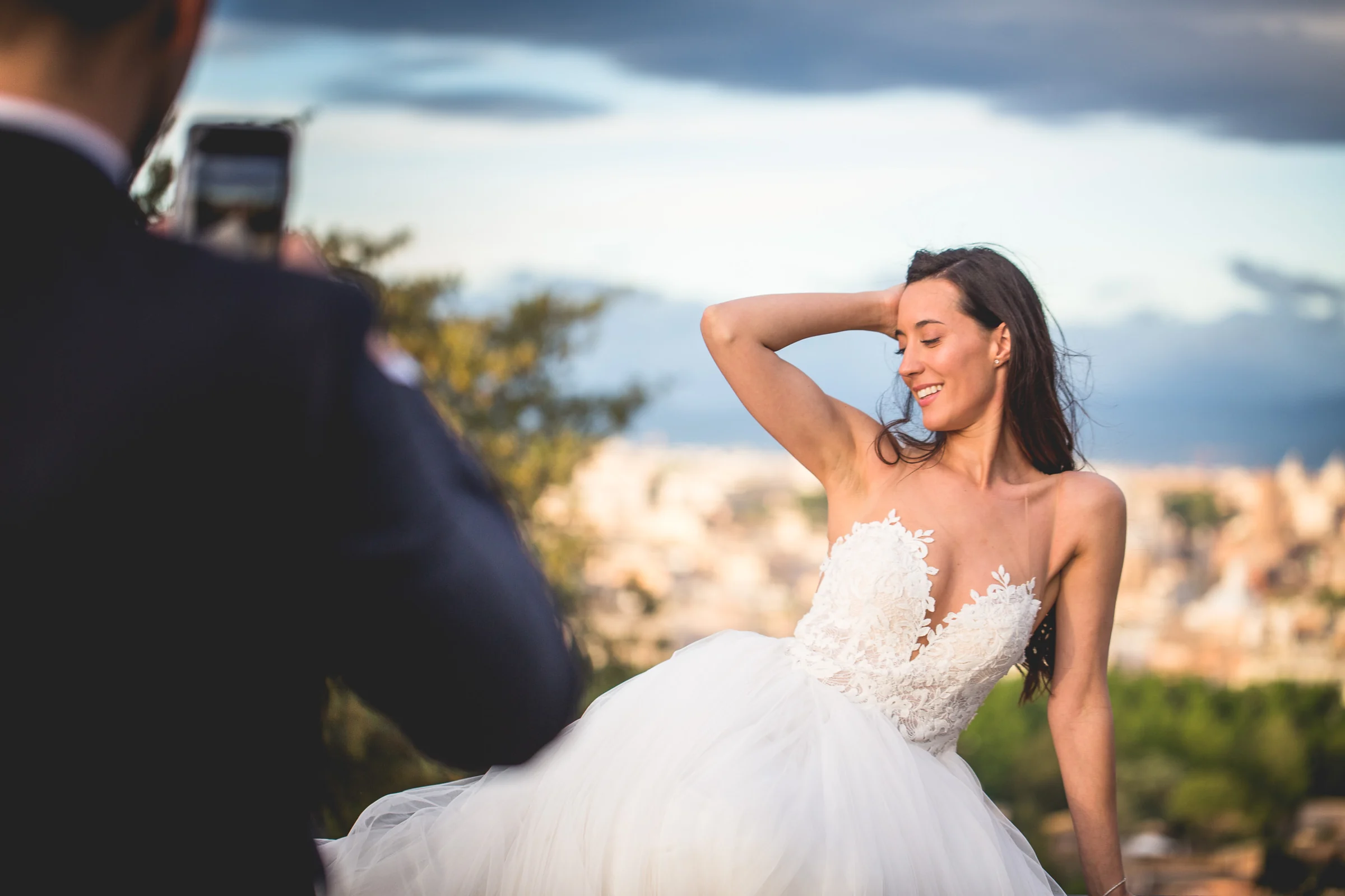 Retrato de la novia sentada en un mirador con el novio desenfocado en primer plano durante una sesión postboda en Miradores y centro histórico de Roma.