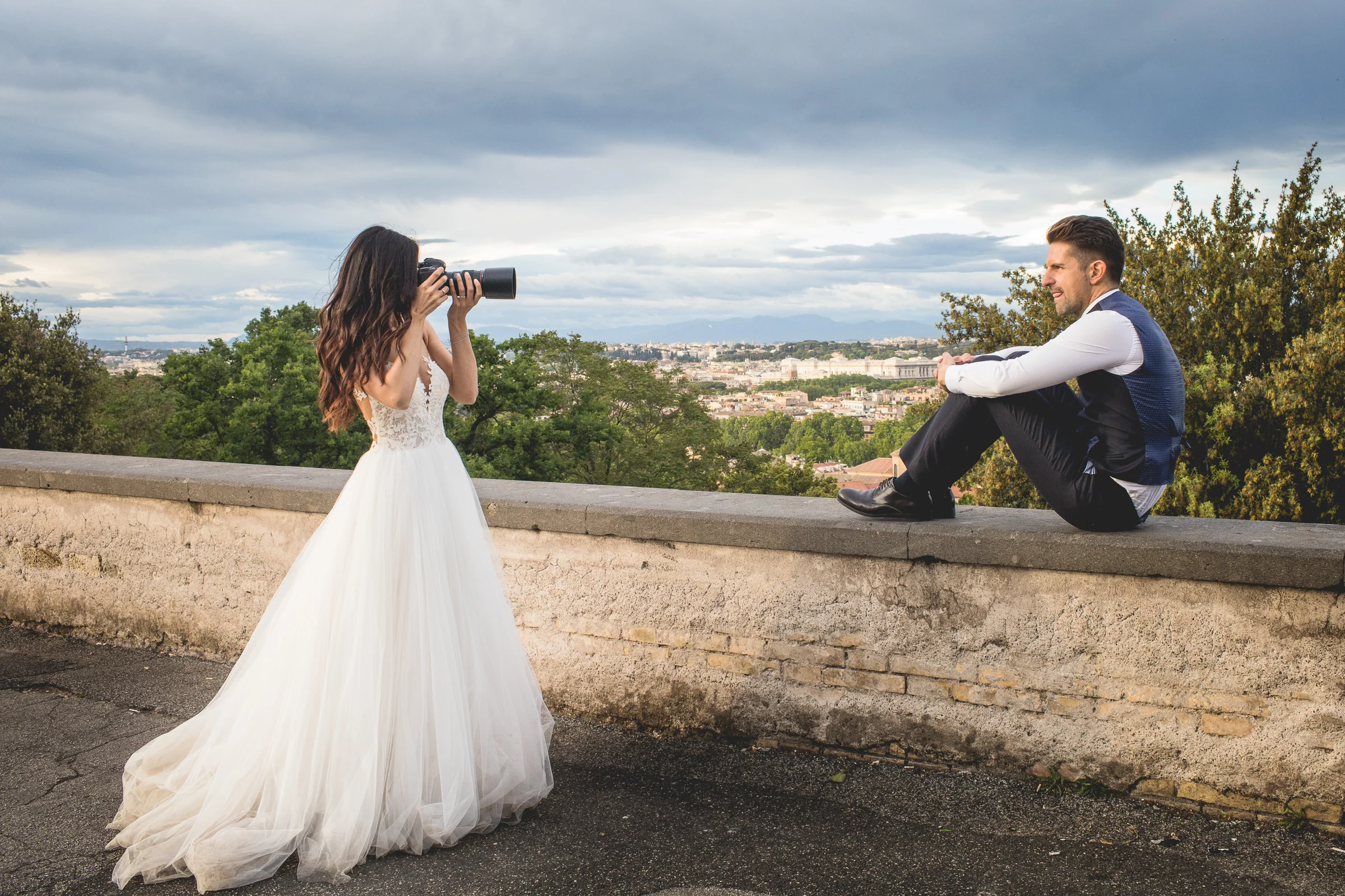 La pareja sentada frente a frente sobre un muro con Roma al fondo durante una sesión postboda en Miradores y centro histórico de Roma.