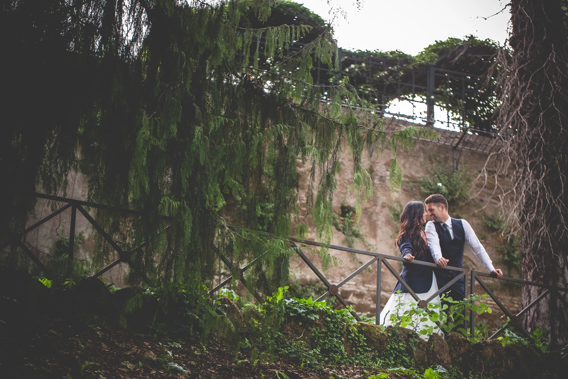 Los novios se abrazan en una escalera exterior rodeada de árboles durante una sesión postboda en Miradores y centro histórico de Roma.