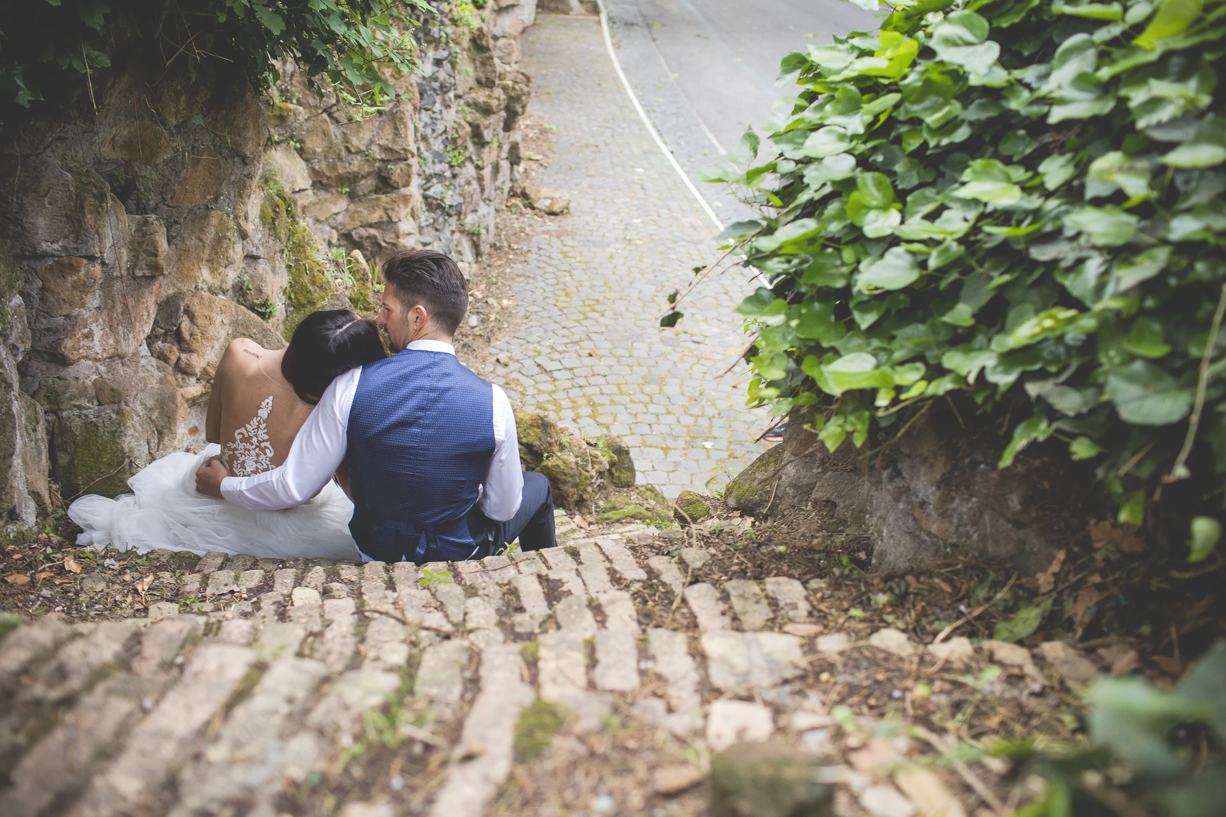 La pareja sentada en una escalinata de piedra vista desde arriba durante una sesión postboda en Miradores y centro histórico de Roma.