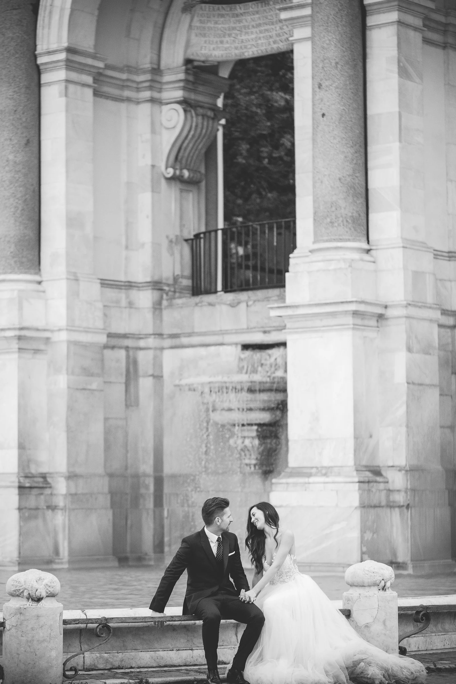 Retrato en blanco y negro de los novios sentados junto a columnas monumentales durante una sesión postboda en Miradores y centro histórico de Roma.