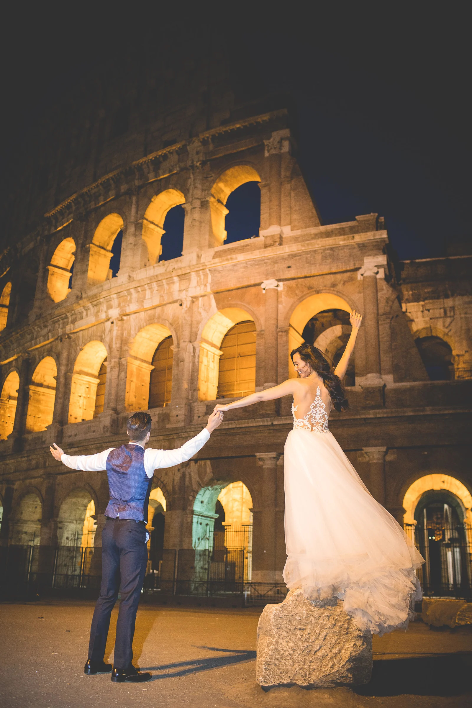 La pareja baila frente al Coliseo iluminado durante la noche durante una sesión postboda en Coliseo de Roma de noche.