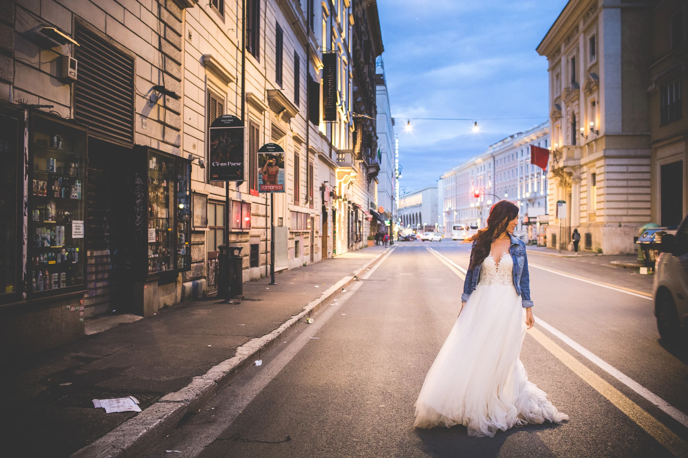 La novia camina sola por una calle de Roma al anochecer con el vestido de boda durante una sesión postboda en Centro histórico de Roma.