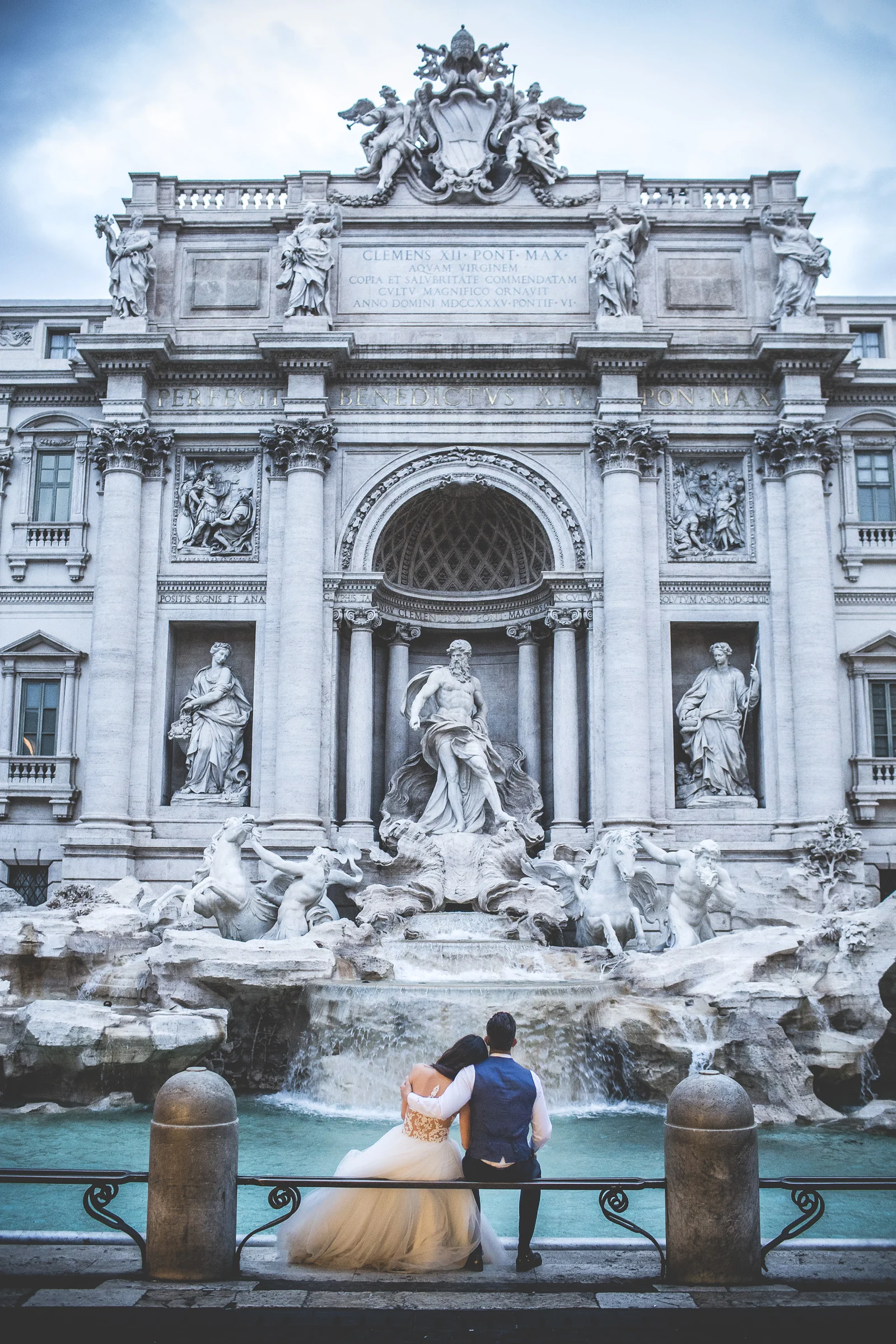 La pareja sentada de espaldas contemplando la Fontana di Trevi durante una sesión postboda en Fontana di Trevi.