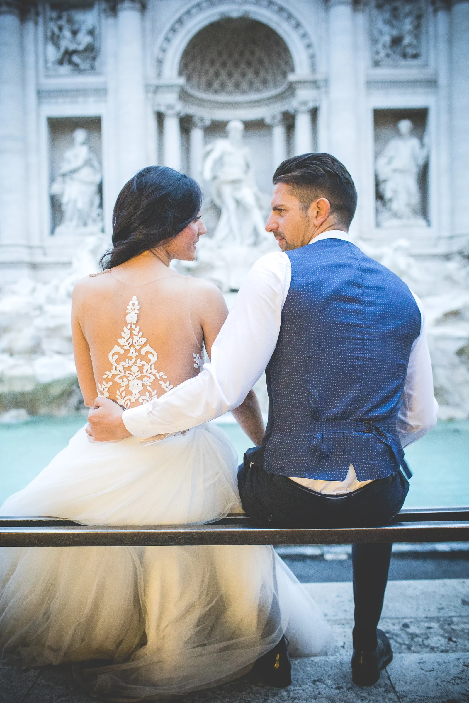Los novios sentados juntos frente a las aguas de la Fontana di Trevi durante una sesión postboda en Fontana di Trevi.