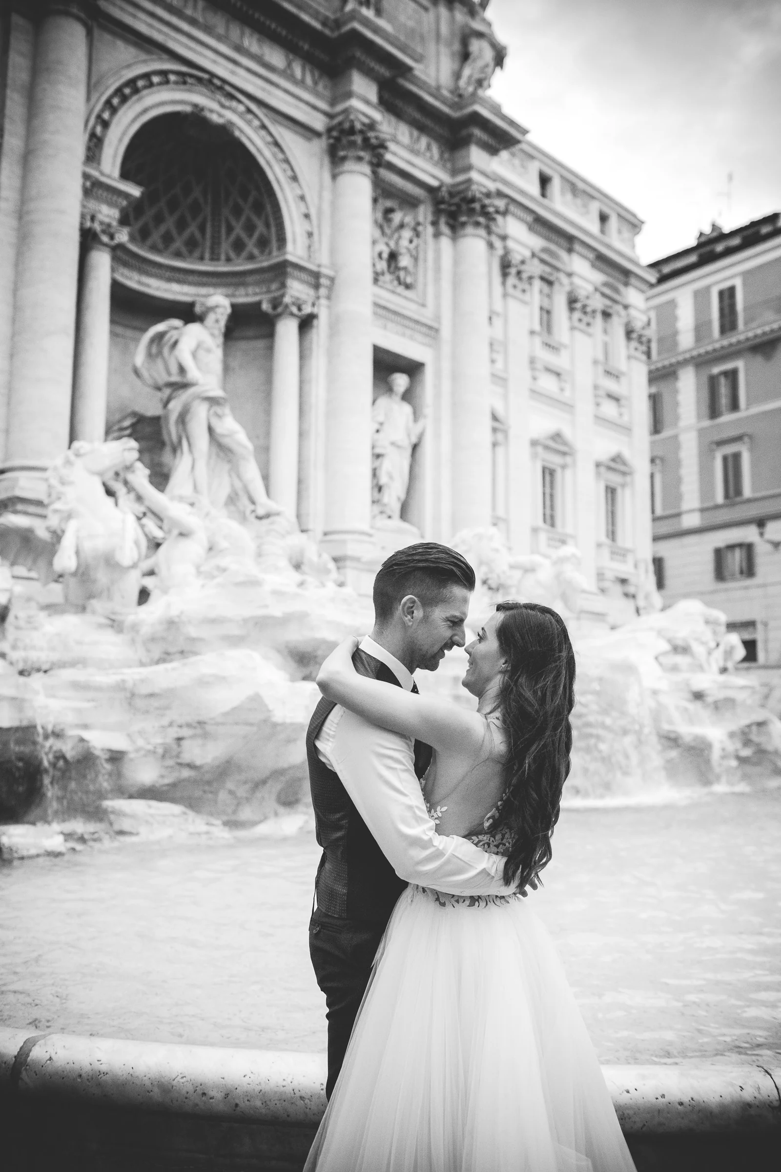 Retrato en blanco y negro de los novios abrazados frente a la Fontana di Trevi durante una sesión postboda en Fontana di Trevi.