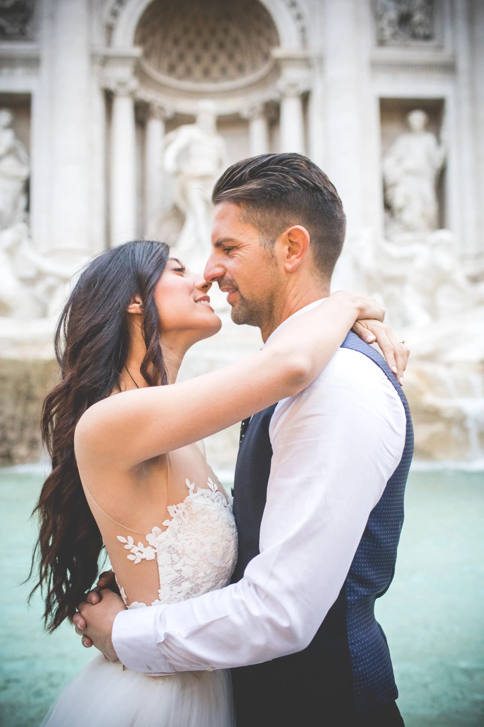 Primer plano de la pareja abrazada con la Fontana di Trevi desenfocada al fondo durante una sesión postboda en Fontana di Trevi.