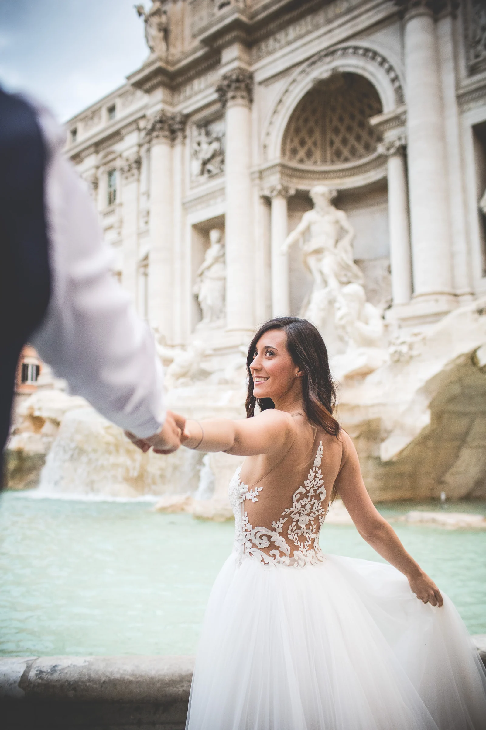 La novia toma la mano del novio frente a la Fontana di Trevi durante una sesión postboda en Fontana di Trevi.