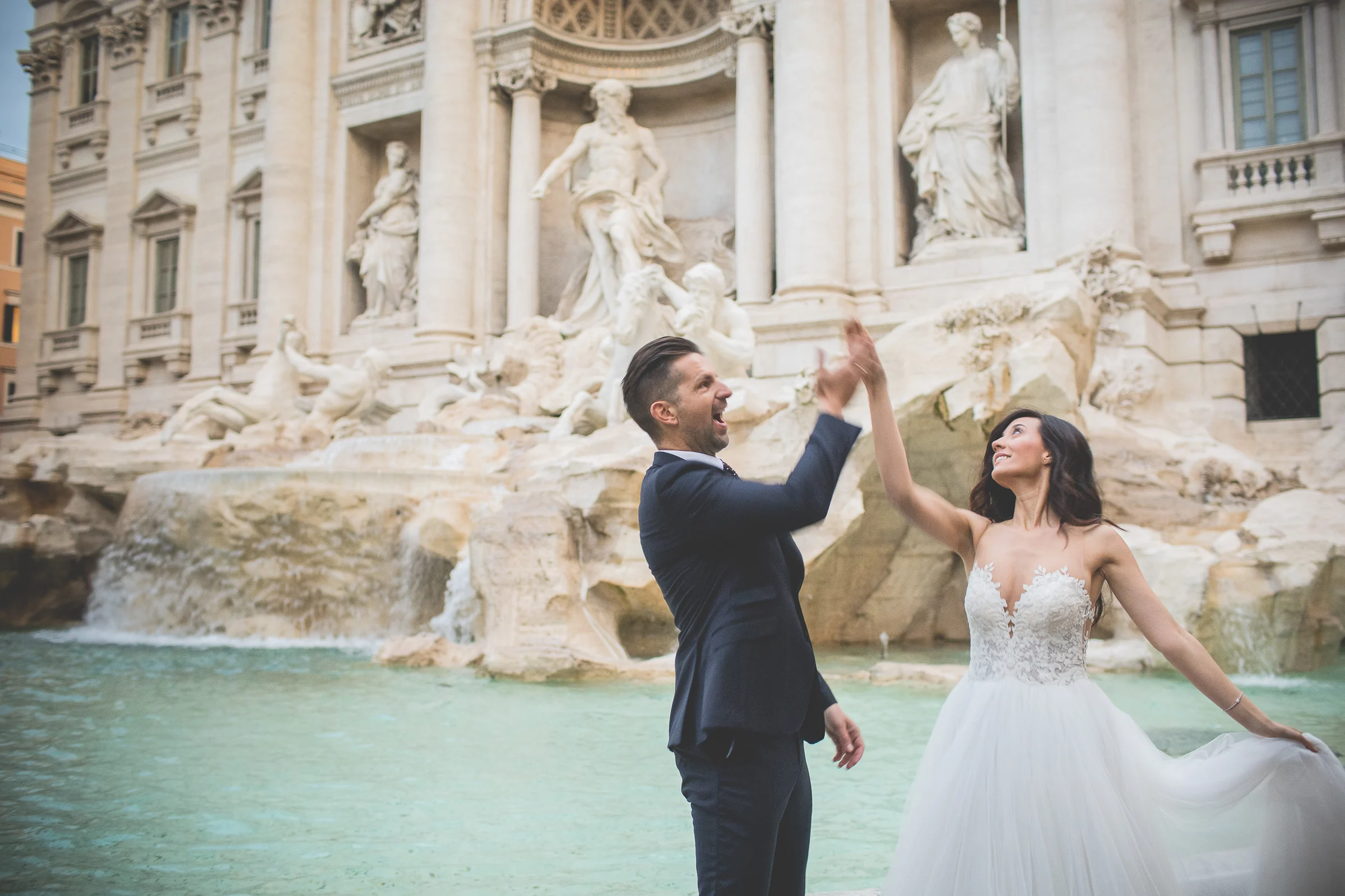 Los novios chocan las manos jugando frente a la Fontana di Trevi durante una sesión postboda en Fontana di Trevi.