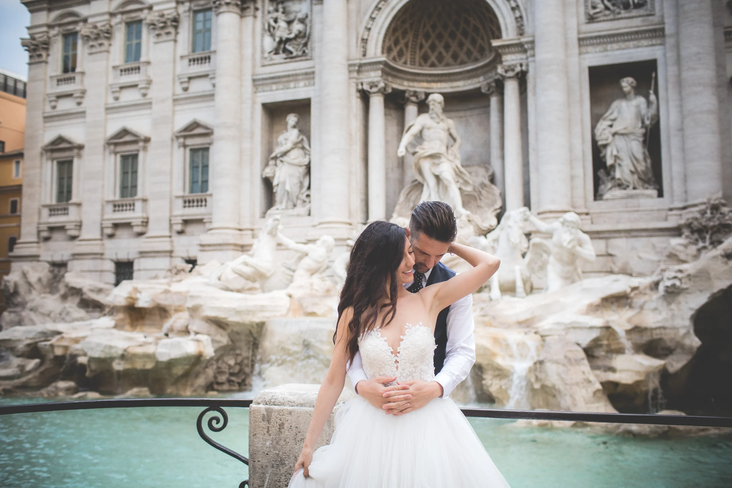 Los novios se abrazan frente a la Fontana di Trevi en un retrato cercano durante una sesión postboda en Fontana di Trevi.